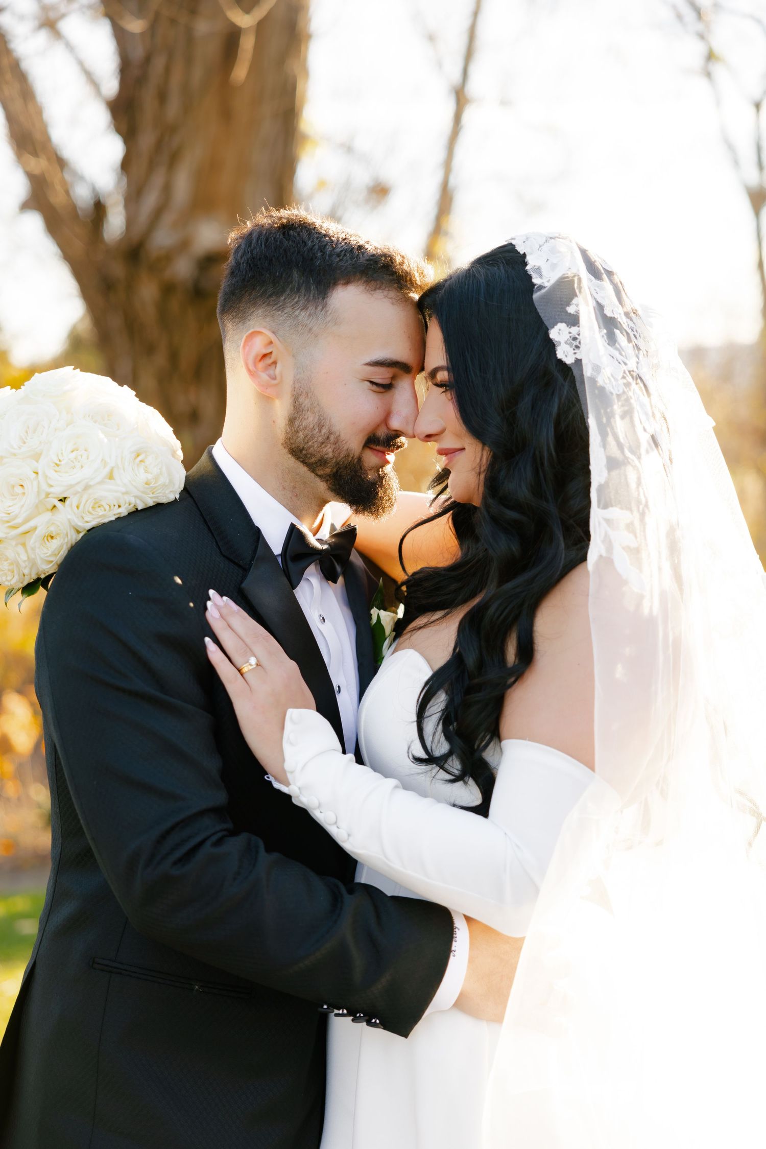 Newlyweds share an intimate moment in golden sunlight with bride in white gown and groom in black tuxedo.