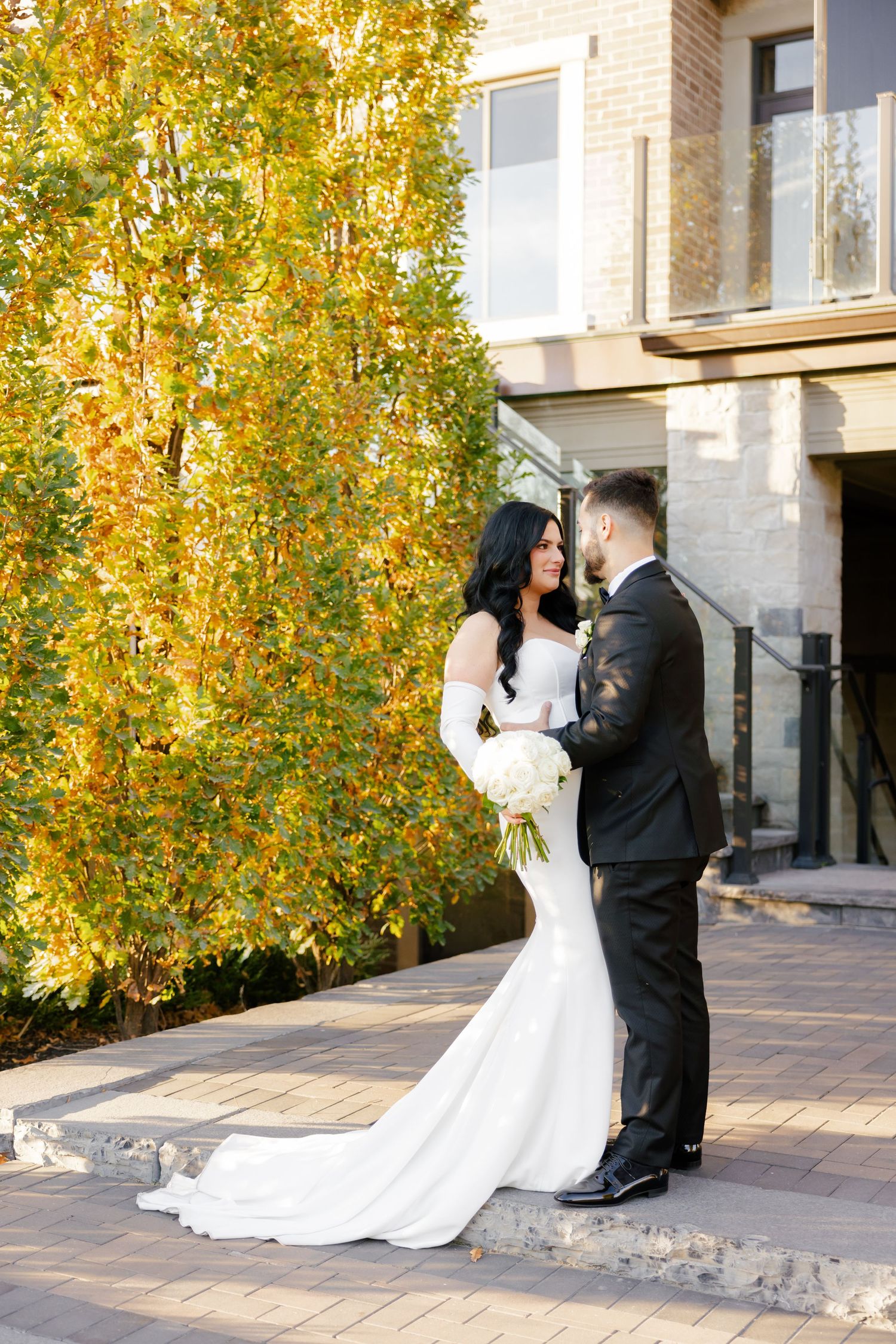 Romantic wedding moment captured against vibrant yellow autumn leaves with bride holding white bouquet.
