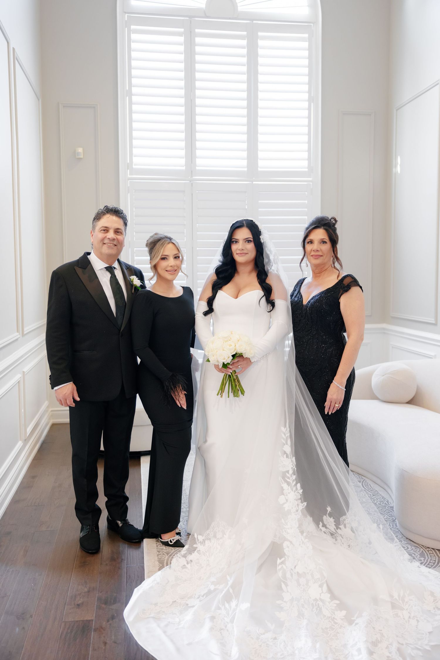 Wedding party poses in elegant formal attire with bride wearing stunning white gown with long train.