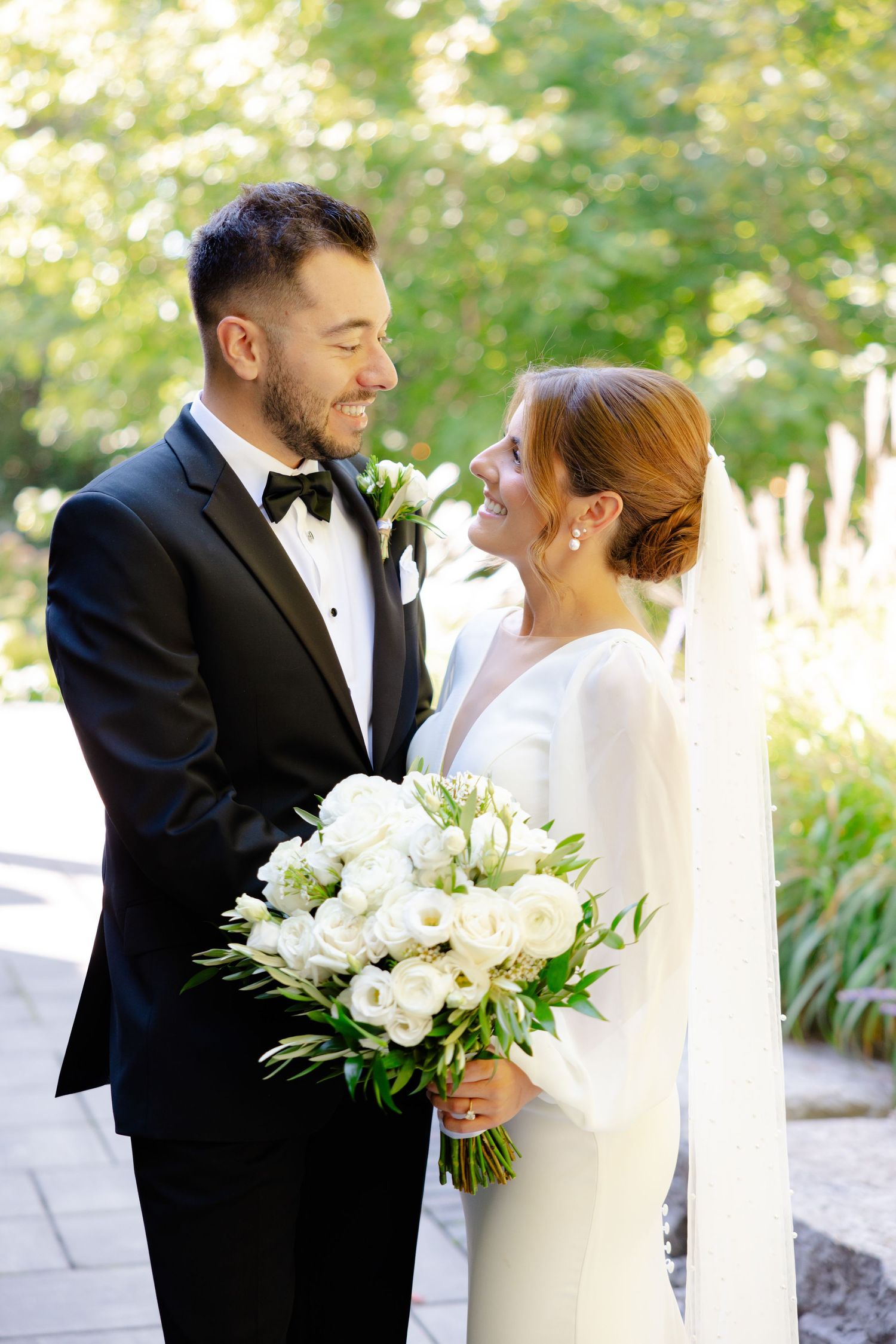 Candid moment of bride and groom sharing a loving gaze in a sunlit garden setting.