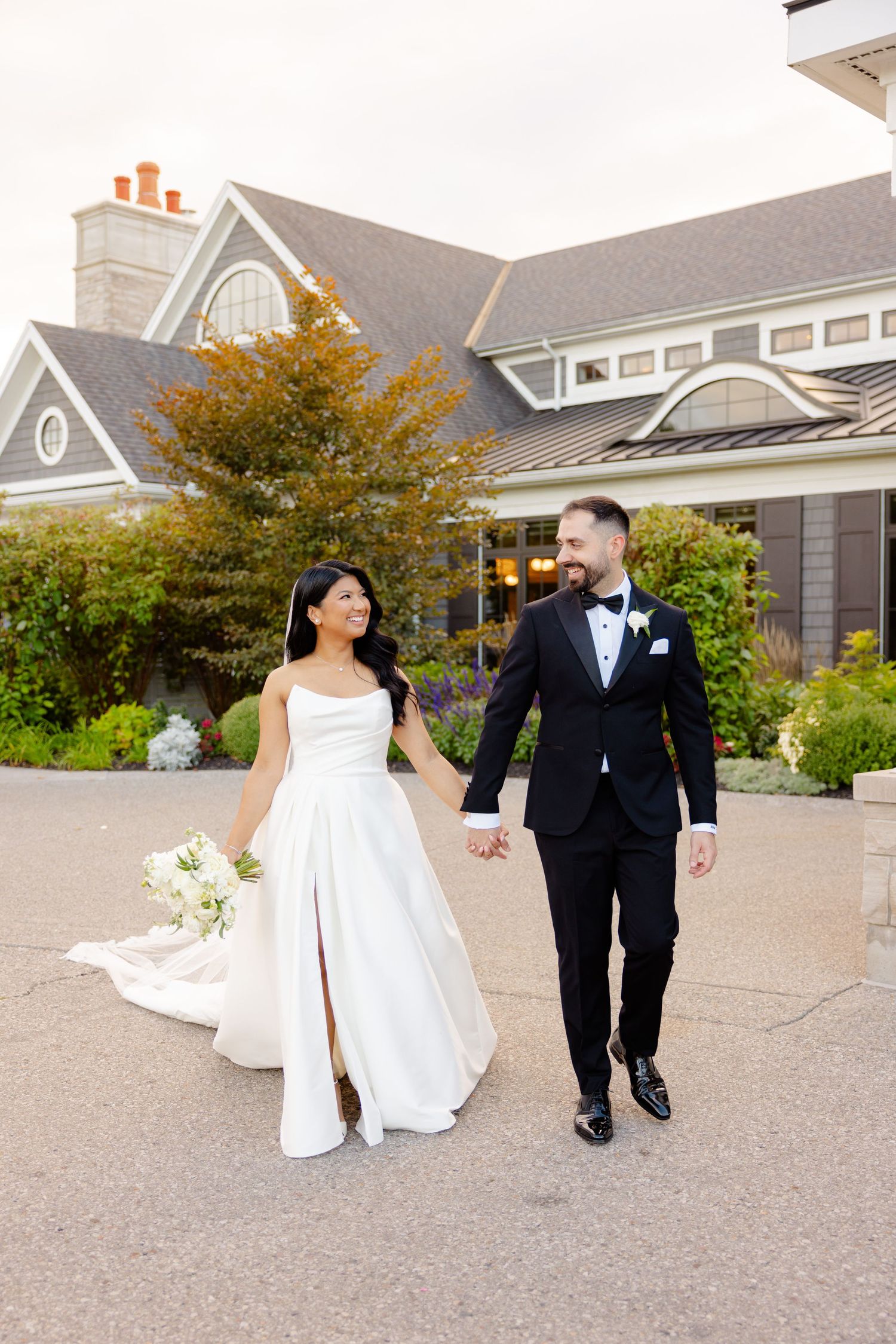Newlyweds hold hands while walking together outside their wedding venue.