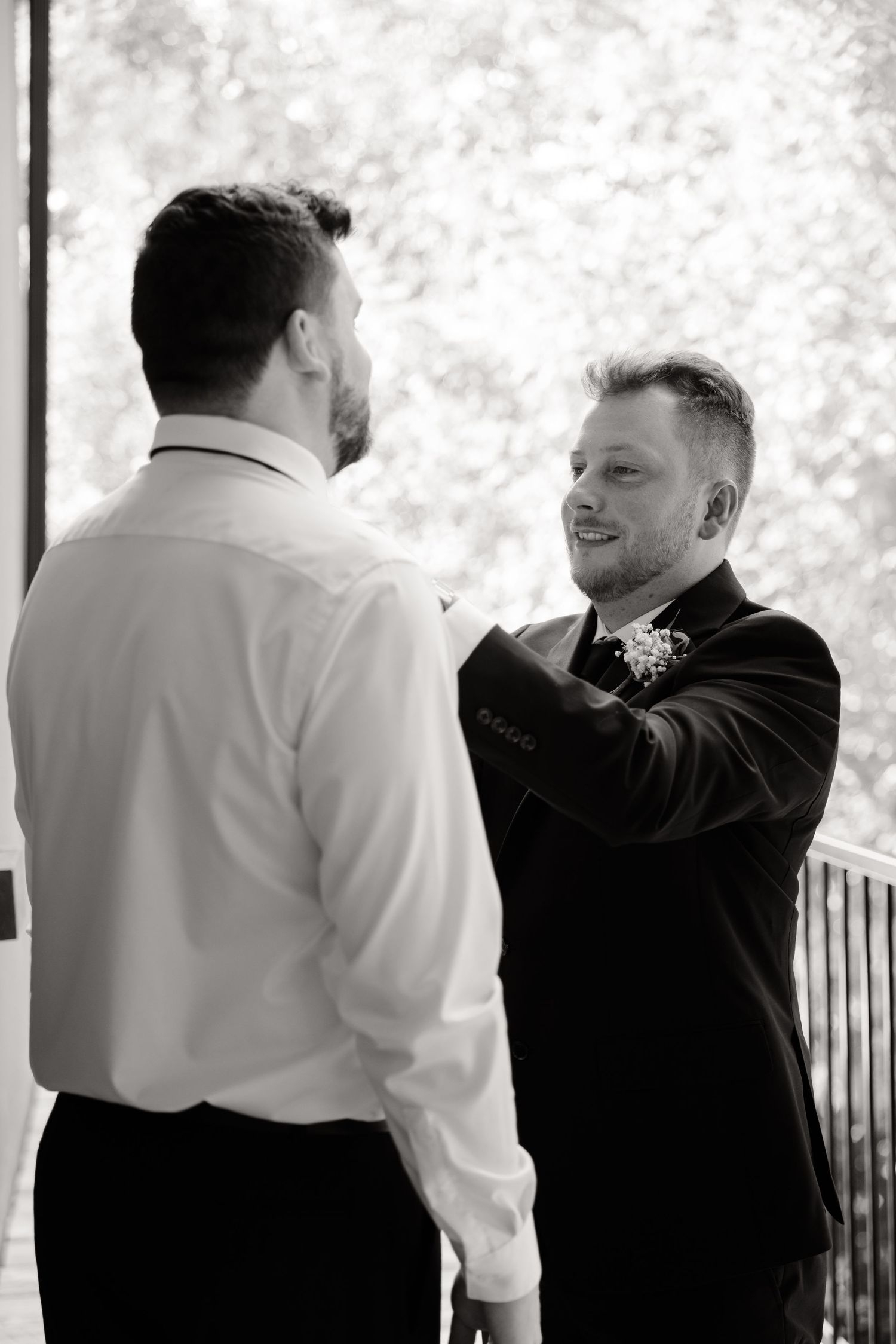 Black and white photo of groomsman helping with formal attire preparations.