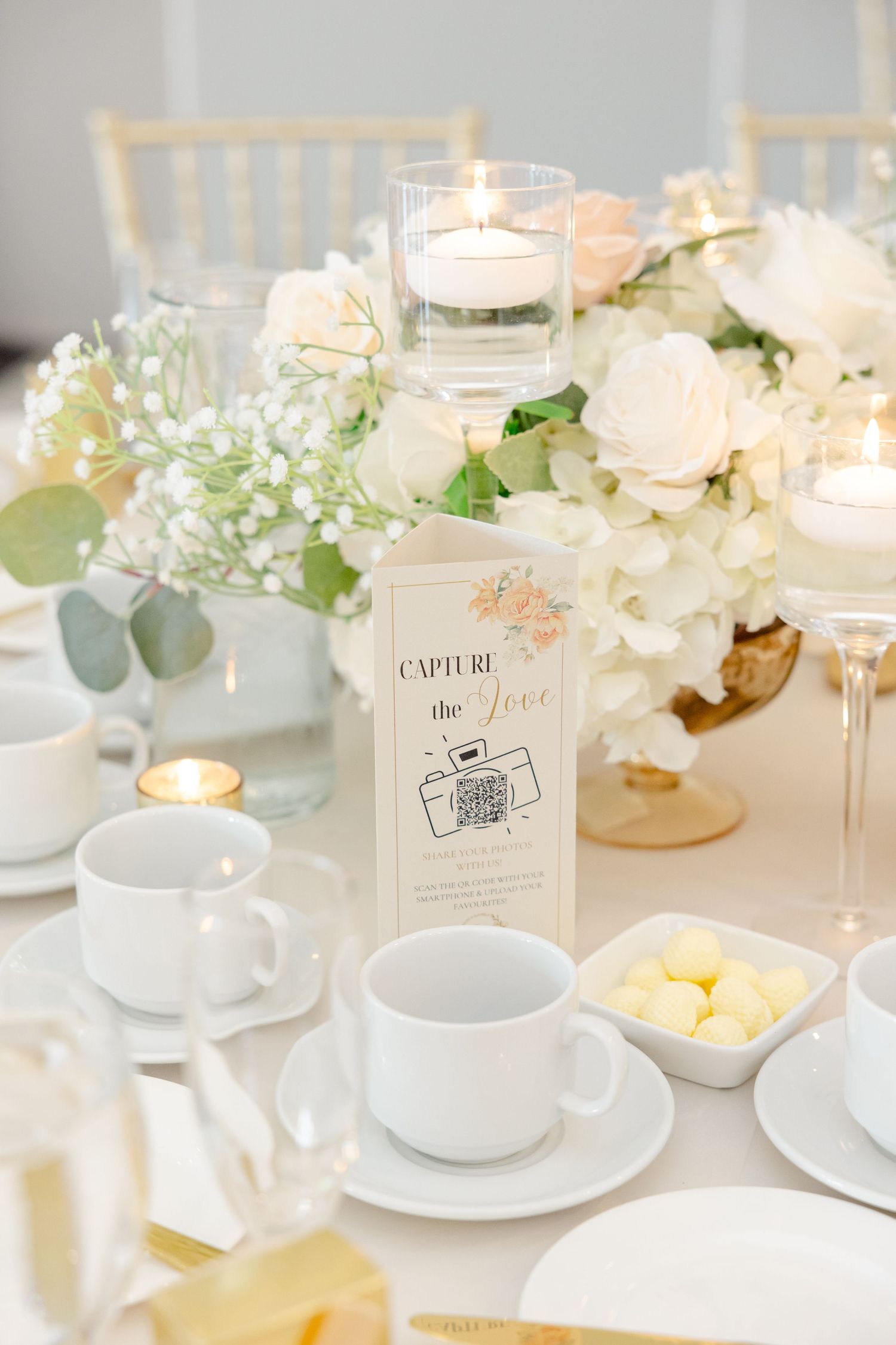 Elegant wedding table setting with white roses, floating candles, and place settings in soft cream tones.