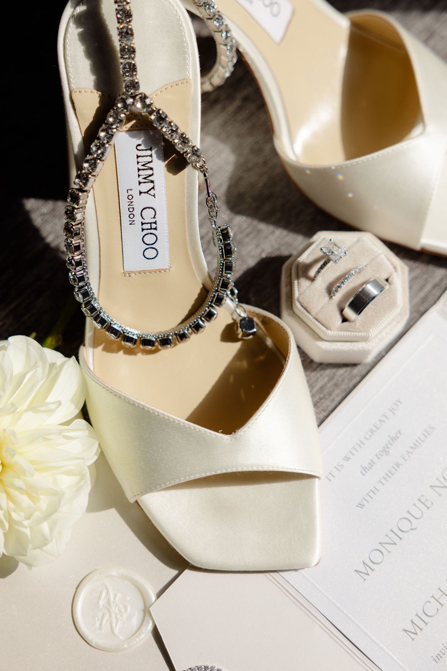 Elegant white Jimmy Choo bridal shoes with crystal details next to wedding stationery.