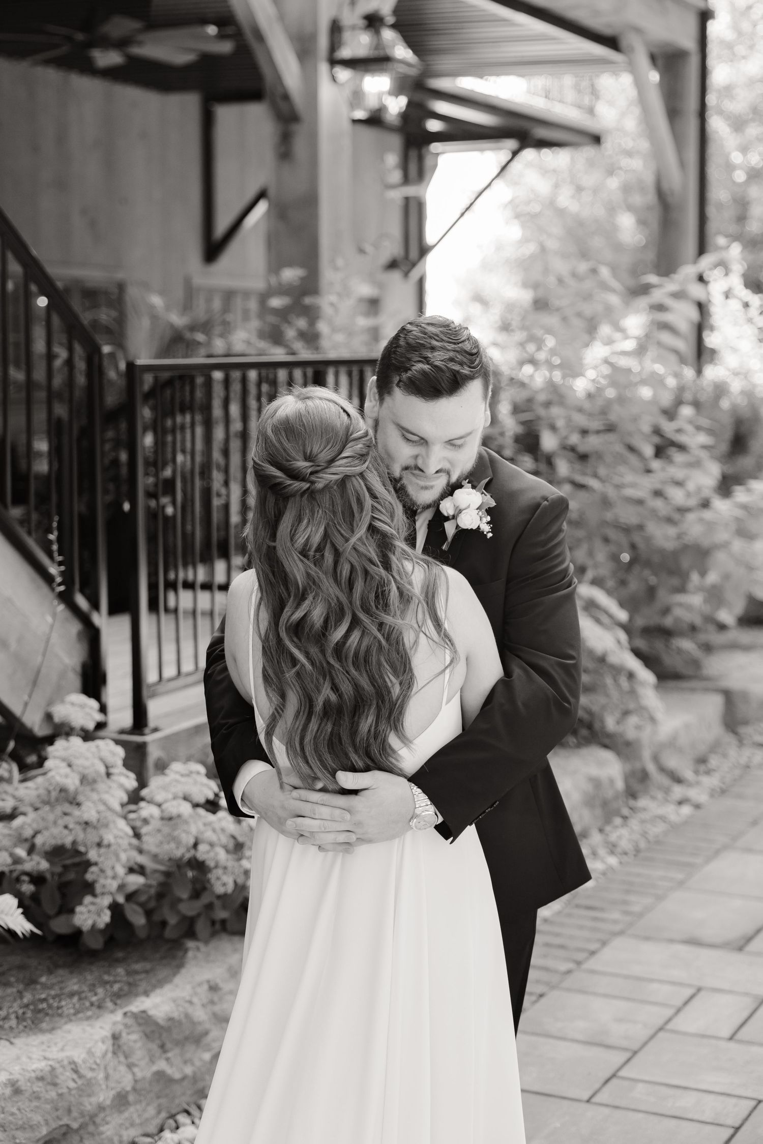 Black and white wedding photo showing a romantic moment on a garden path with stone walls.