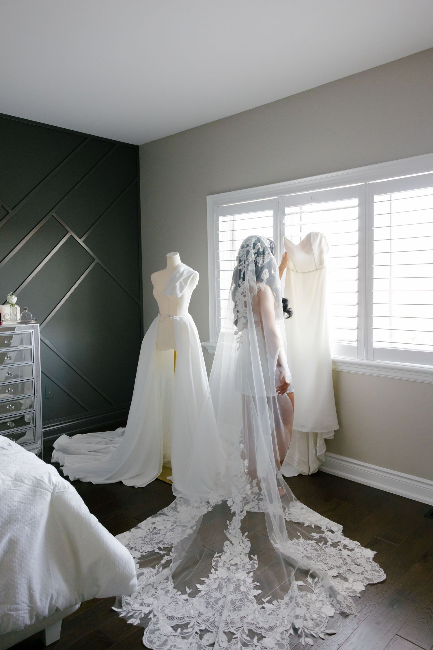 Wedding dress and veil displayed on mannequin near window with geometric accent wall.