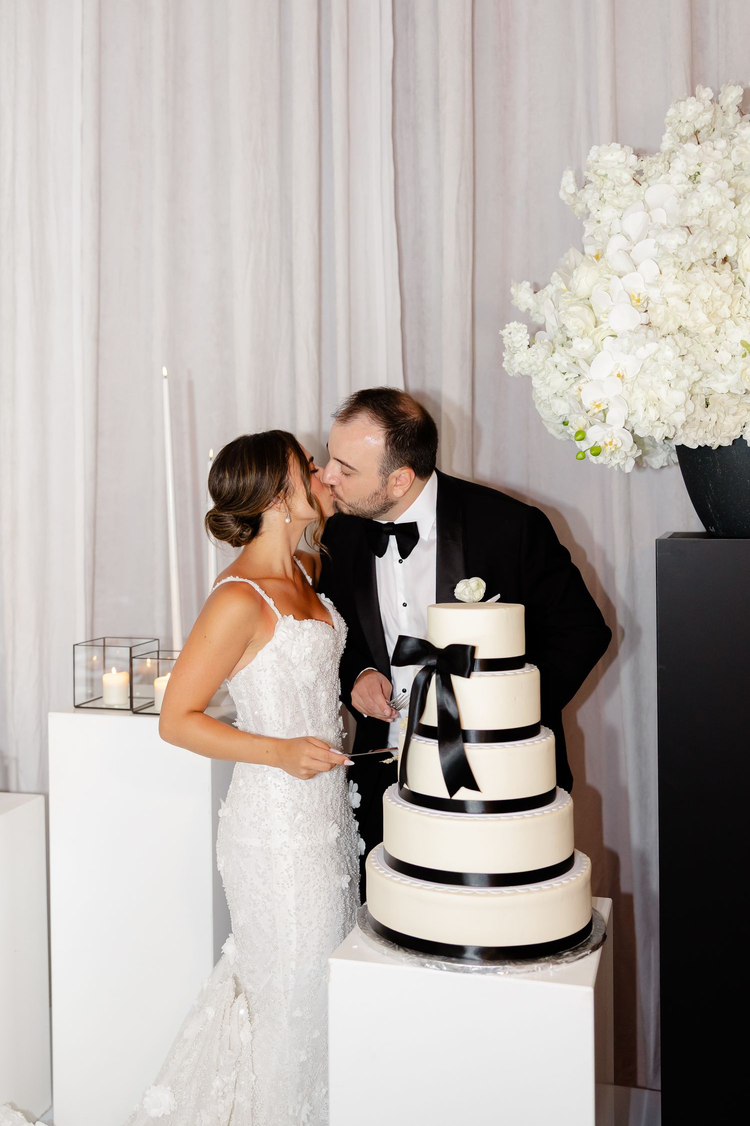 Elegant black and white wedding cake with ribbon details stands beside white hydrangea arrangement at formal reception.