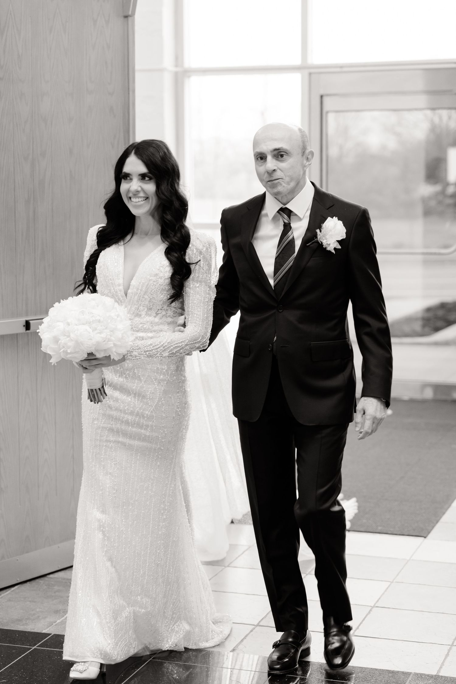 Couple in wedding attire walks together in formal black and white portrait.