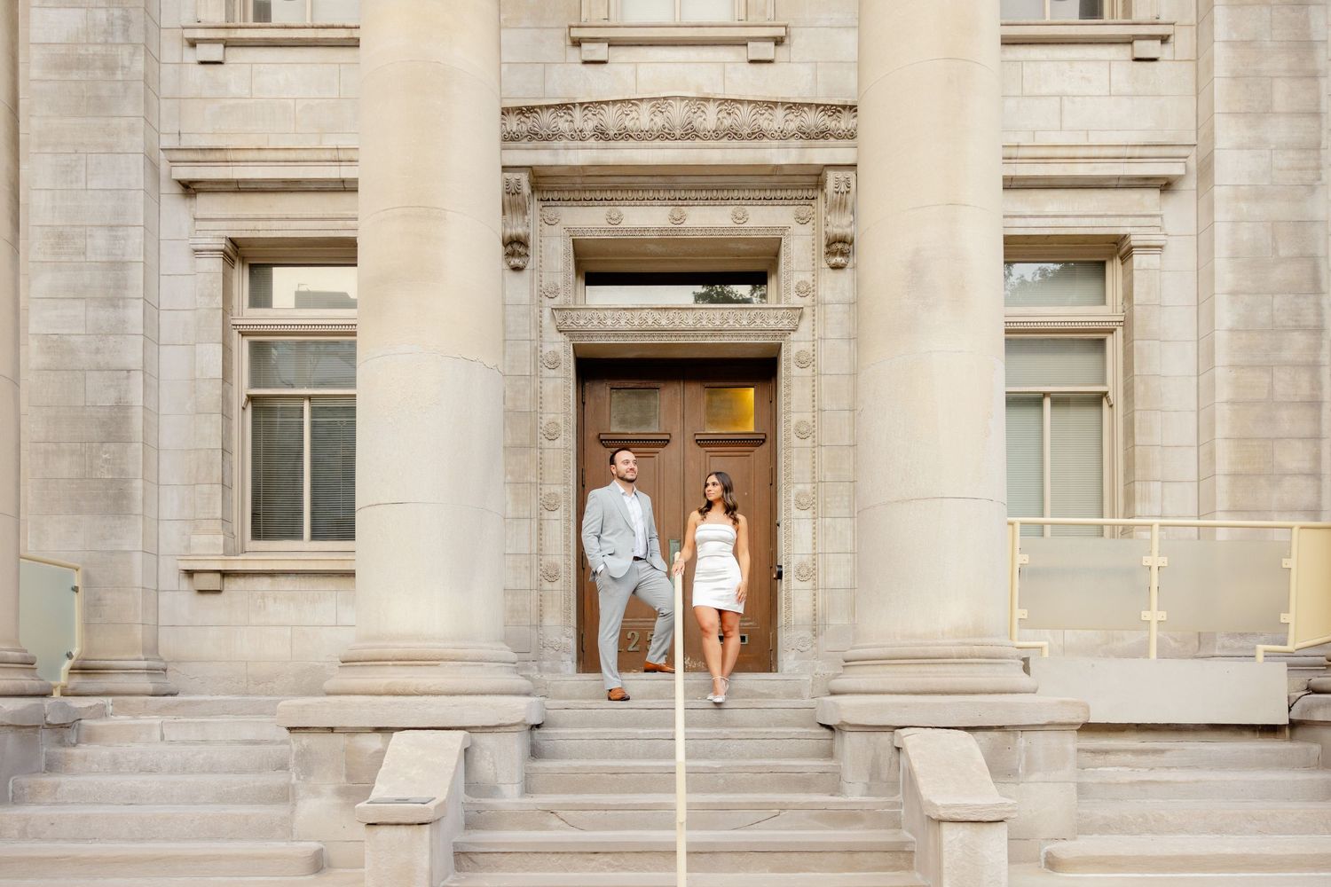 A couple stands in a grand doorway of a classical stone building with columns.
