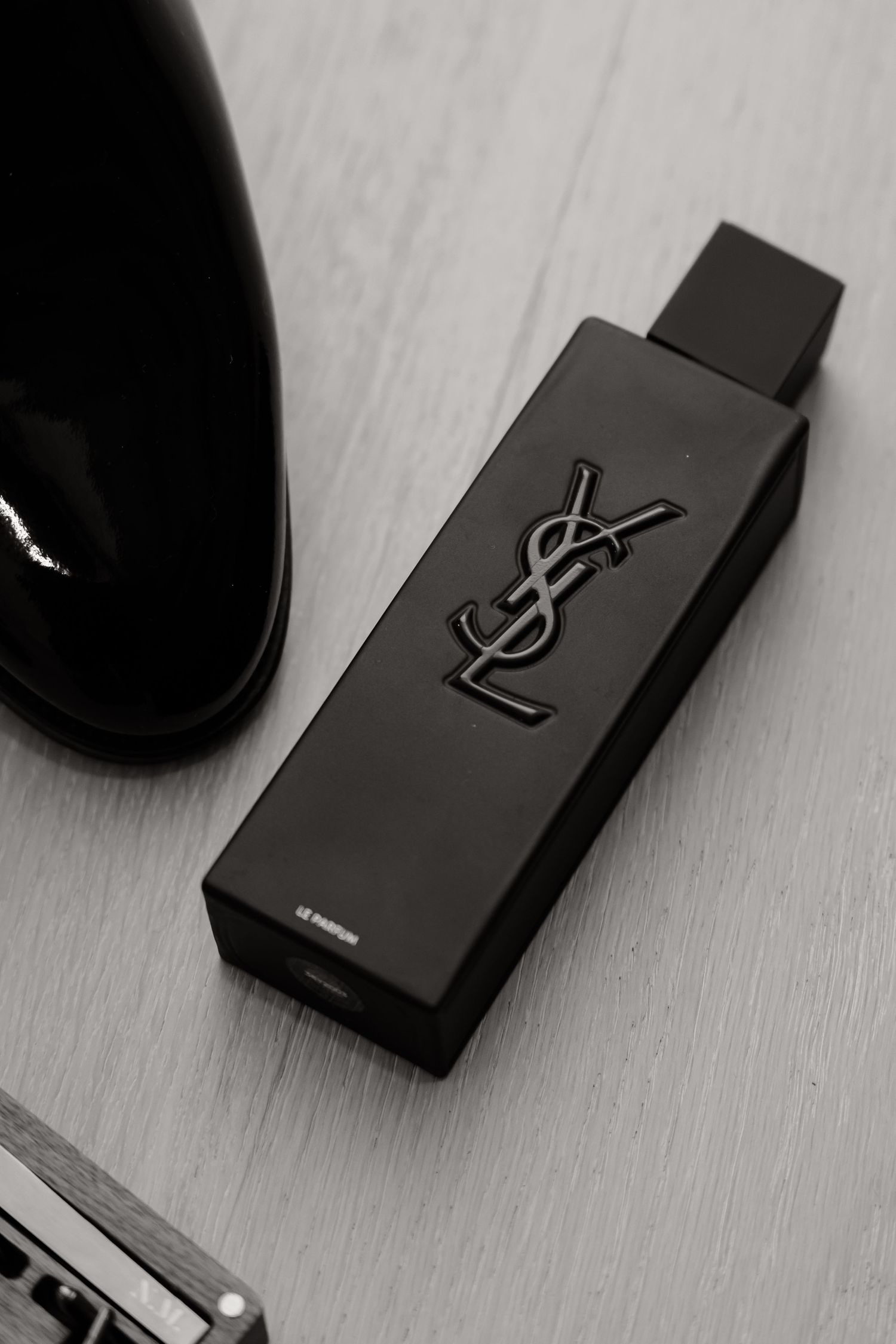 Black YSL branded perfume bottle on wooden surface.