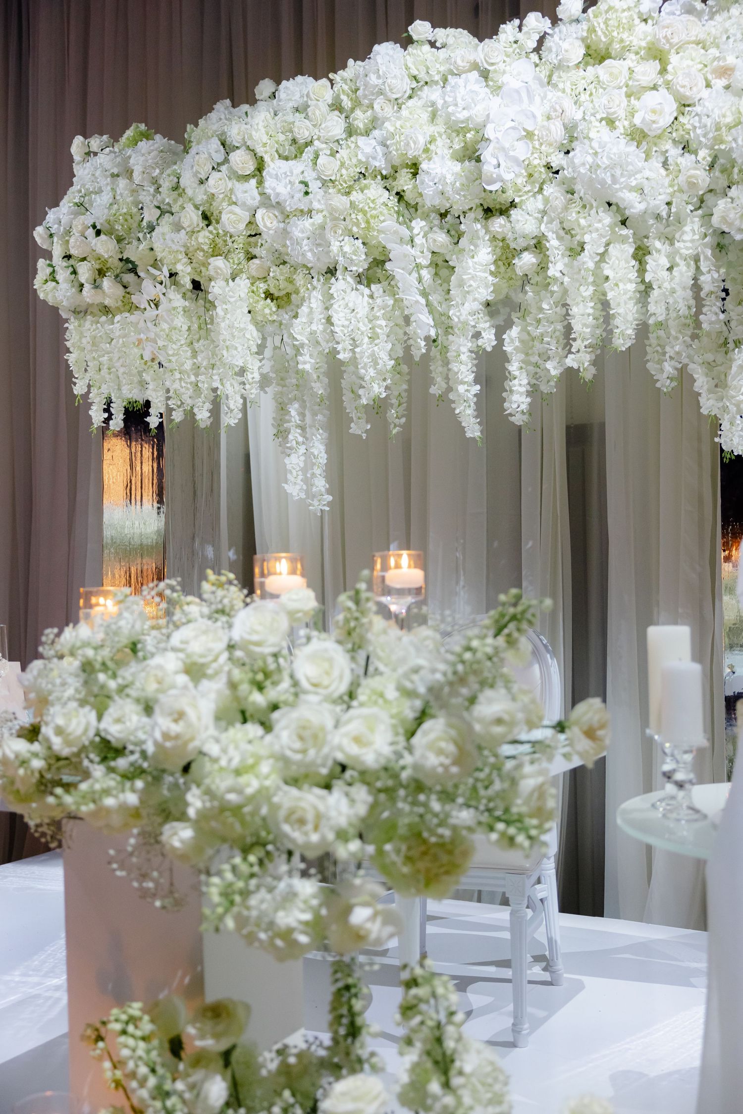 Stunning white floral canopy with cascading flowers and roses over elegant wedding reception setup.