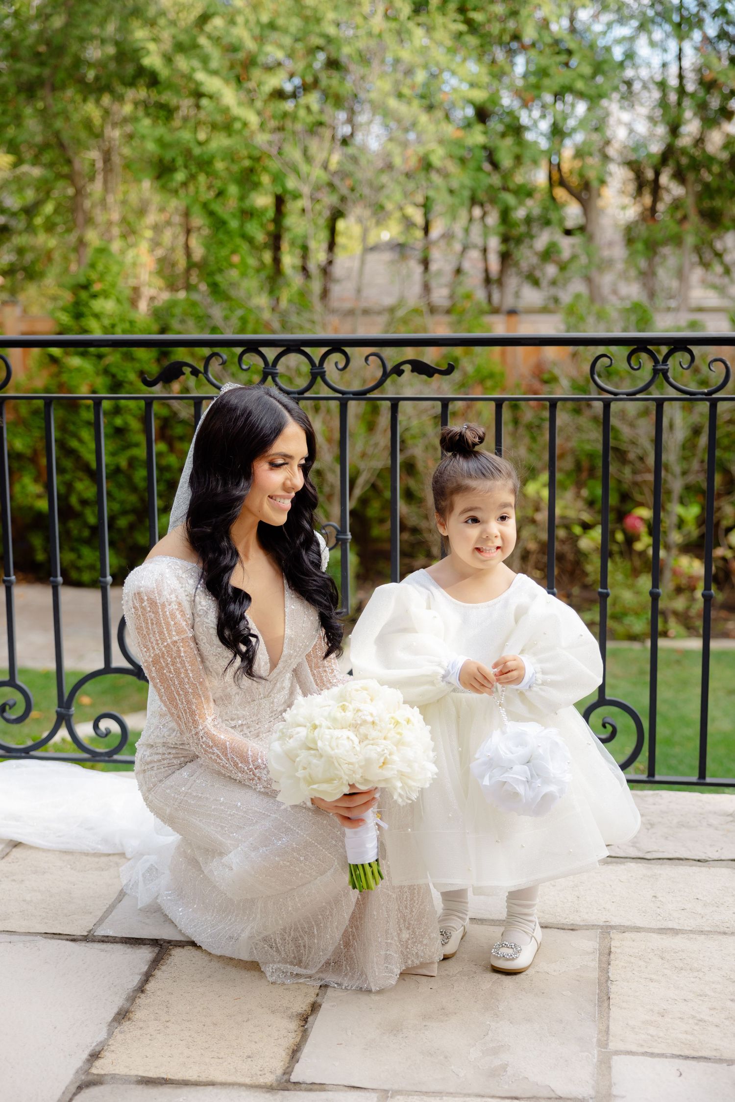 Bride and flower girl share joyful moment while posing with white bouquets on outdoor terrace.