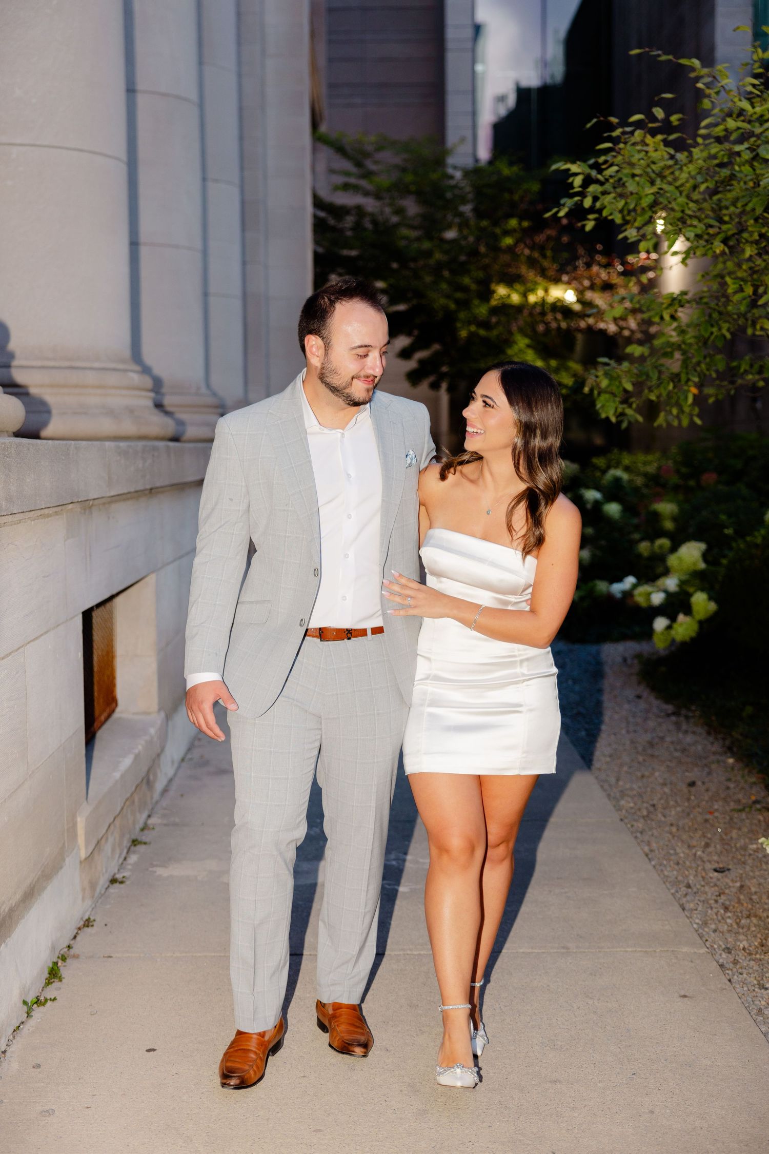 Couple taking romantic evening stroll along building exterior in formal attire.