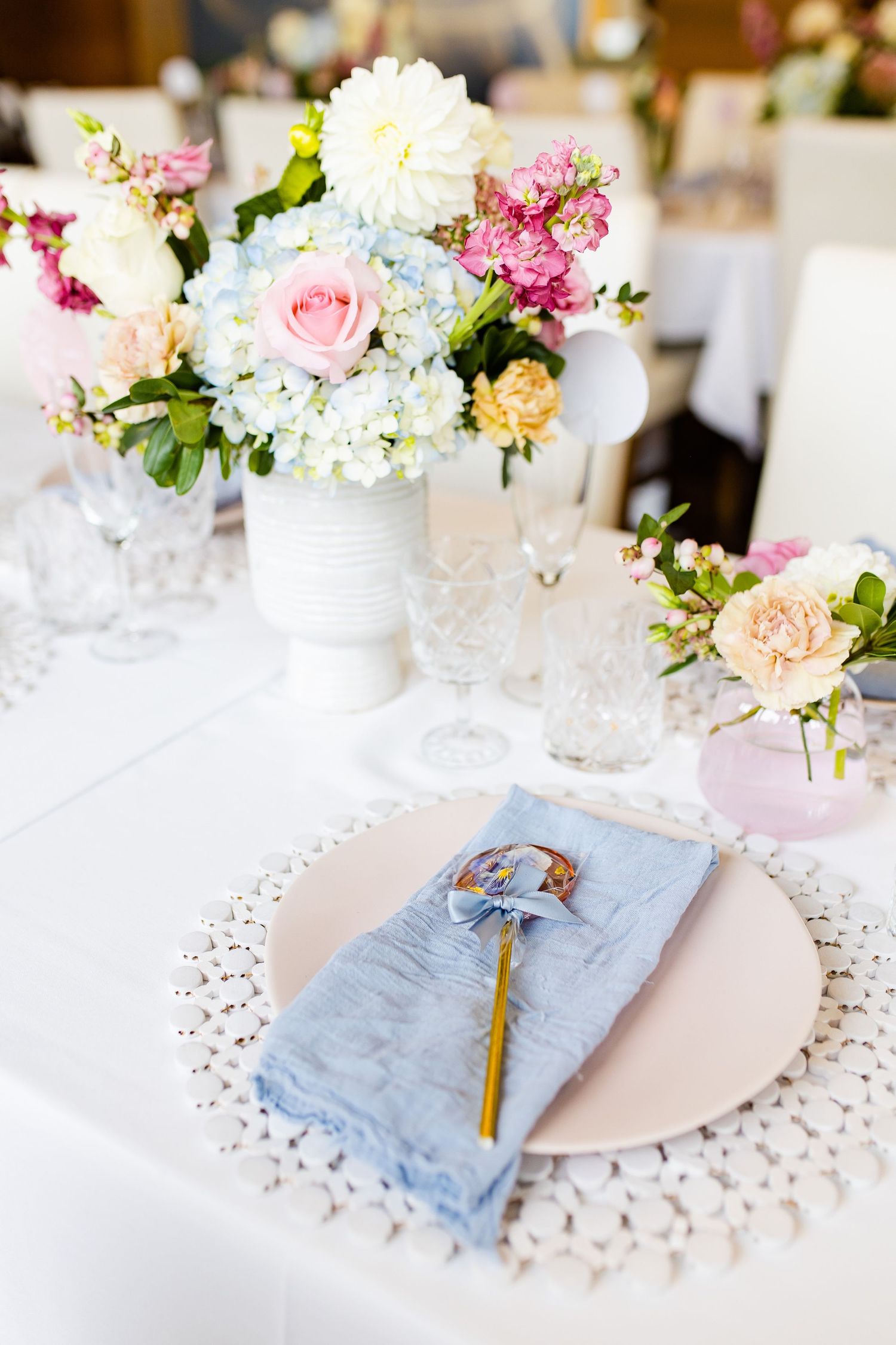 Table setting with pink and white flower arrangement, blue napkin, and lace placemat.