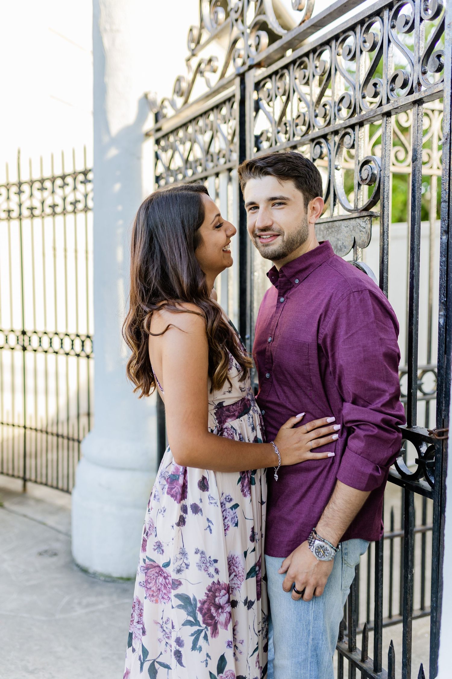 Couple sharing a moment against ornate iron gates, dressed in purple and floral patterns.