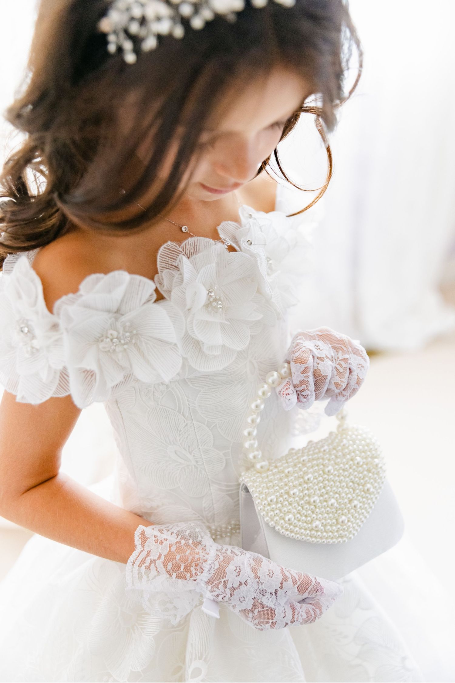 Delicate bridal portrait featuring pearl handbag, lace gloves and floral dress details in soft light.
