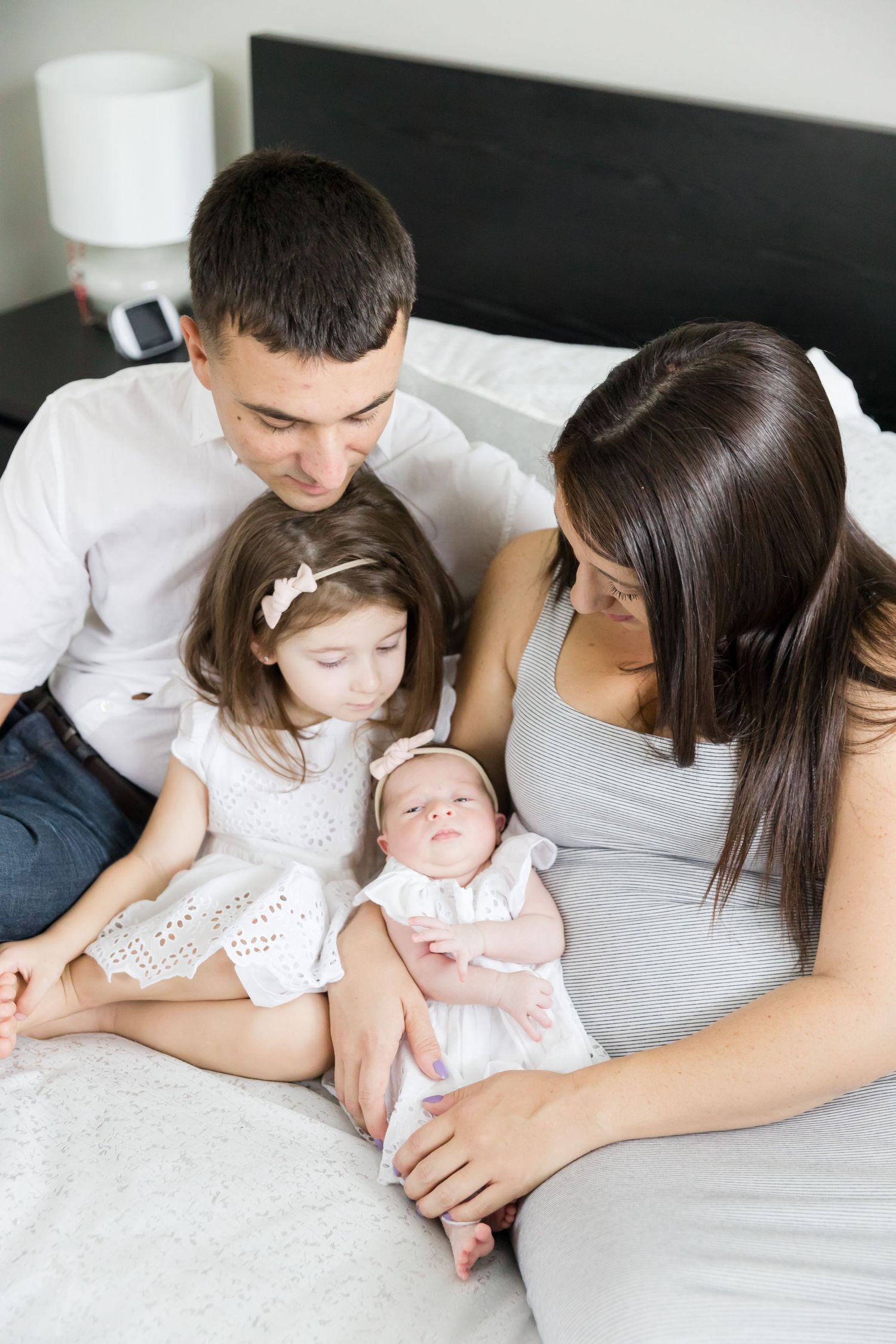 Intimate family moment with parents and children on white bedding.