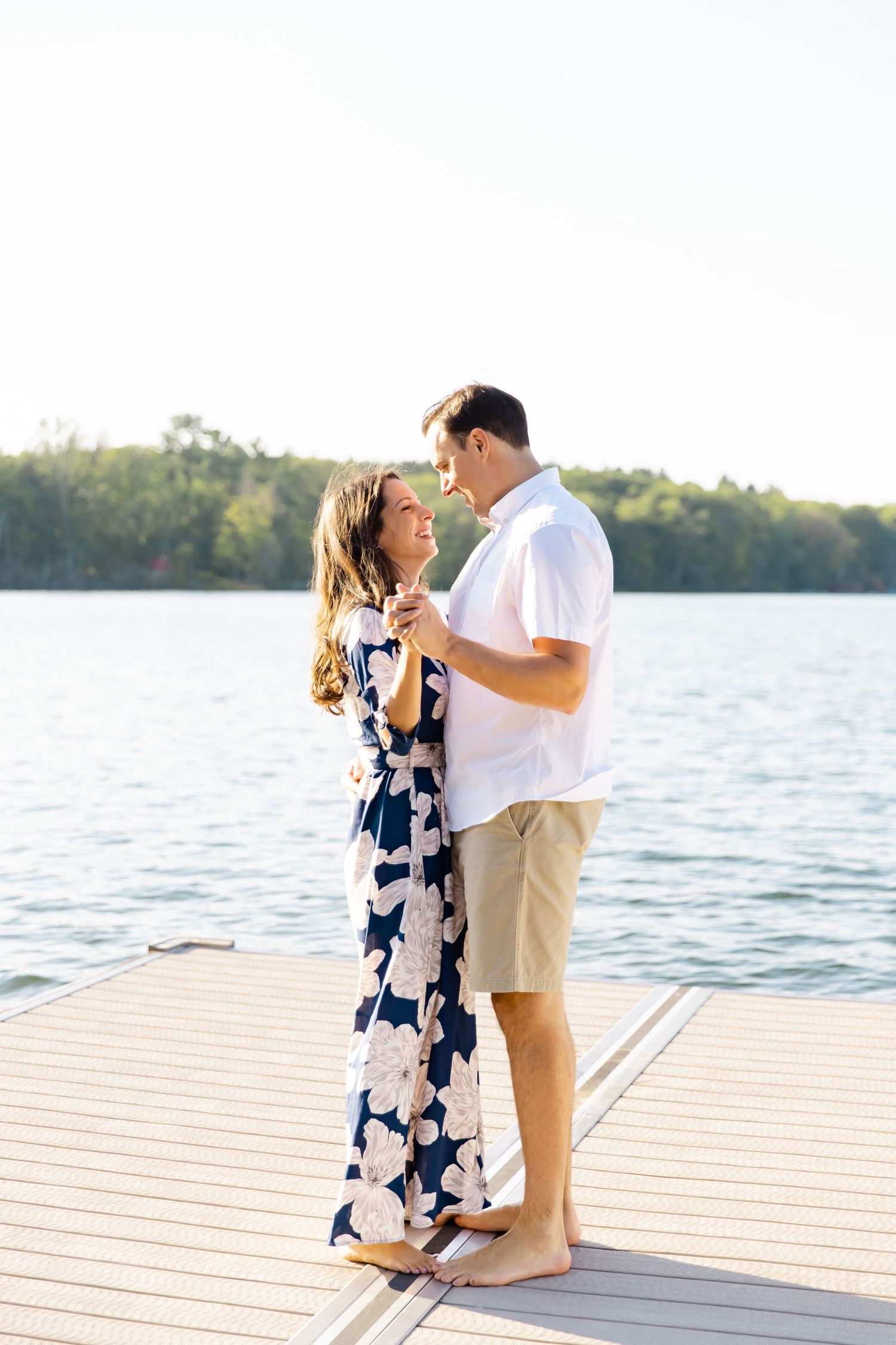 A tender moment shared between a couple on a wooden dock overlooking a serene lake.