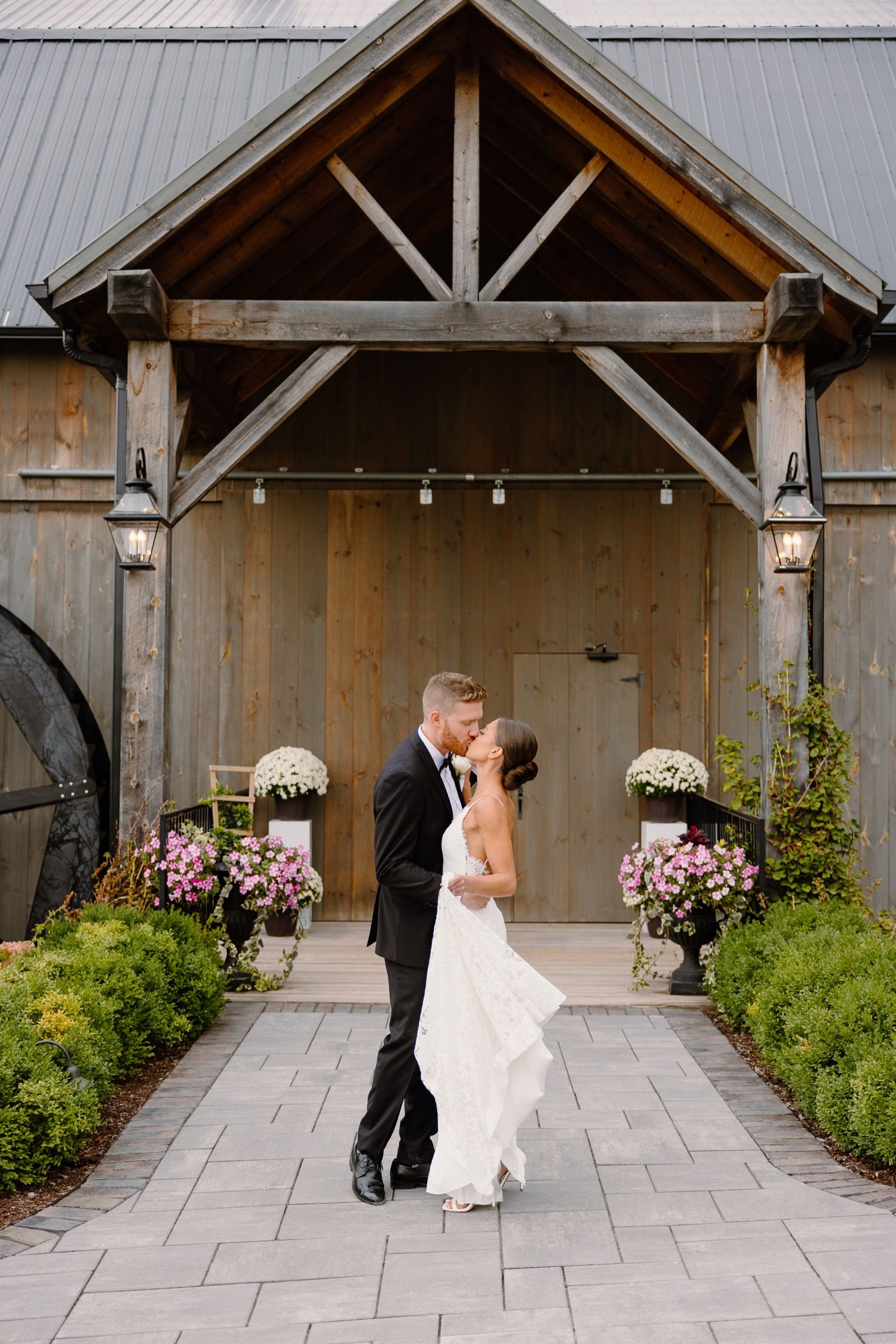 Stone pathway leading to rustic barn entrance decorated with floral arrangements creates perfect ceremony setting.