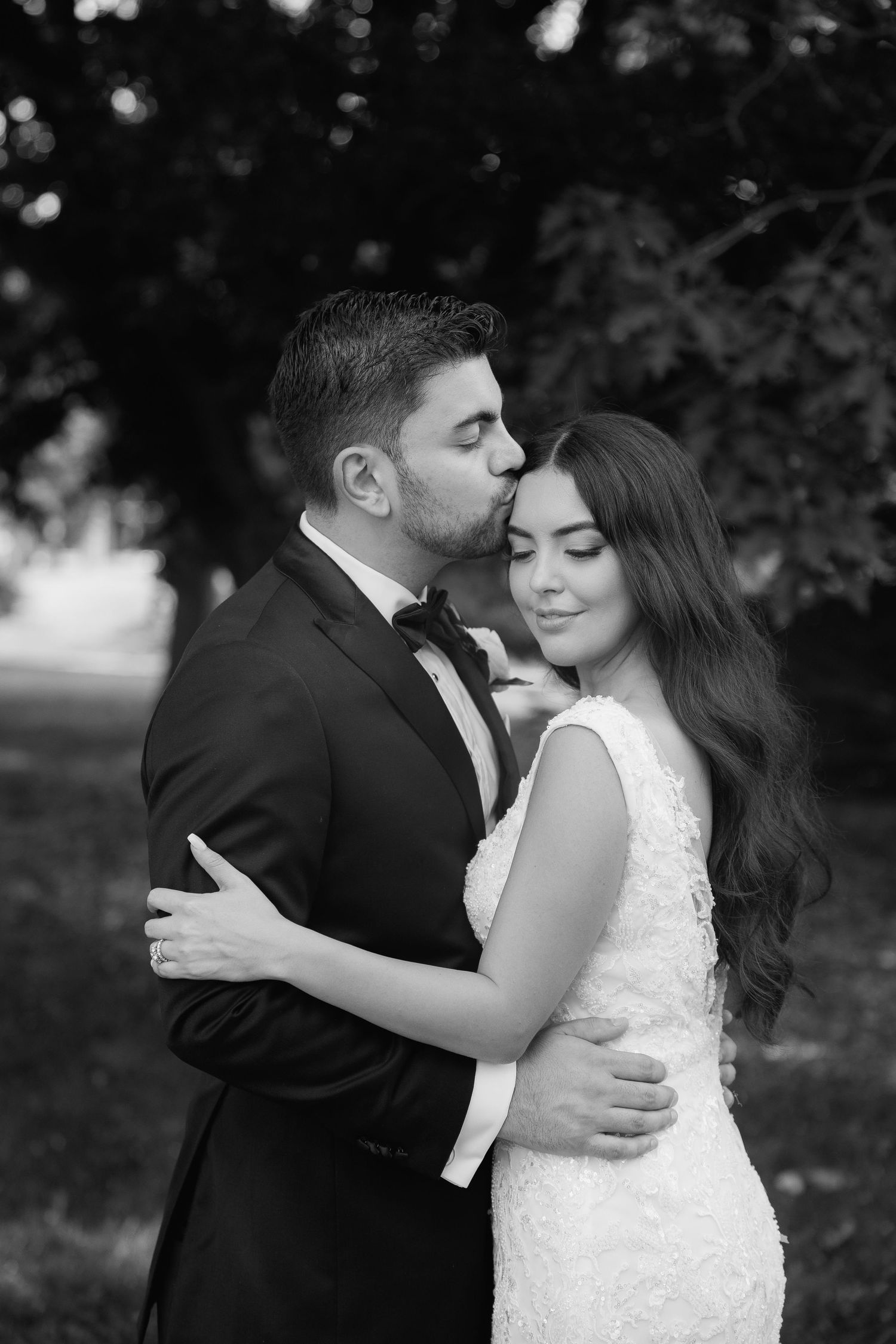 Black and white portrait of newlyweds sharing an intimate moment against a natural backdrop.