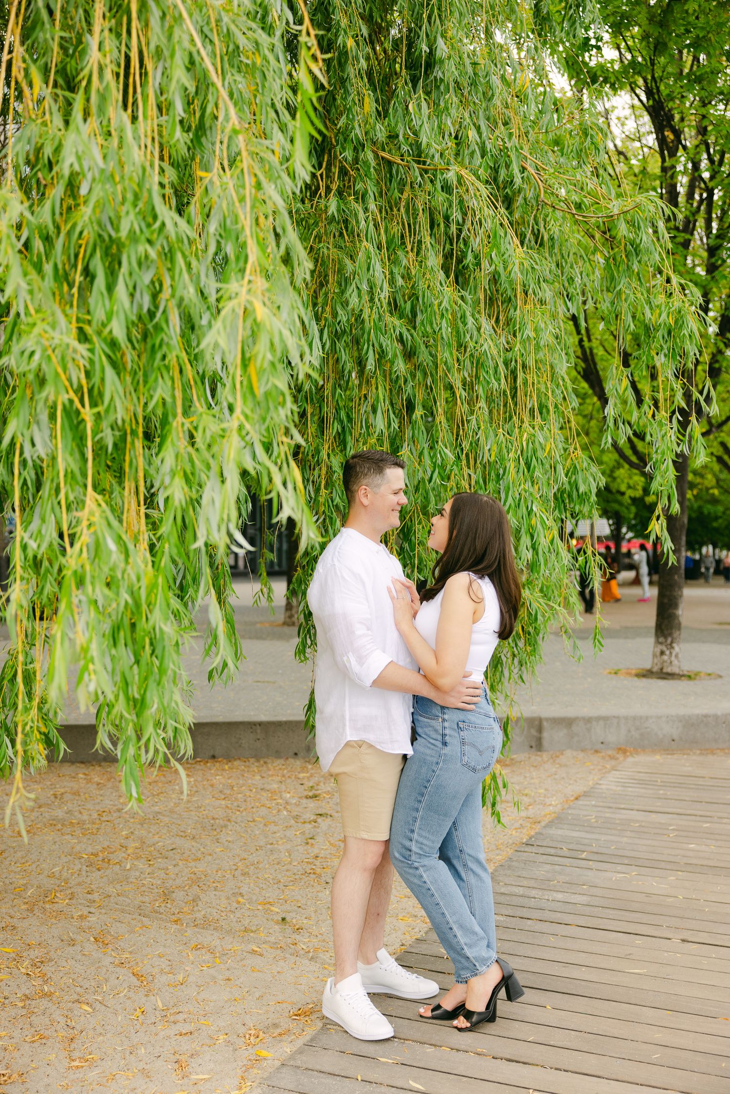 Couple sharing tender moment on wooden boardwalk surrounded by willow trees.