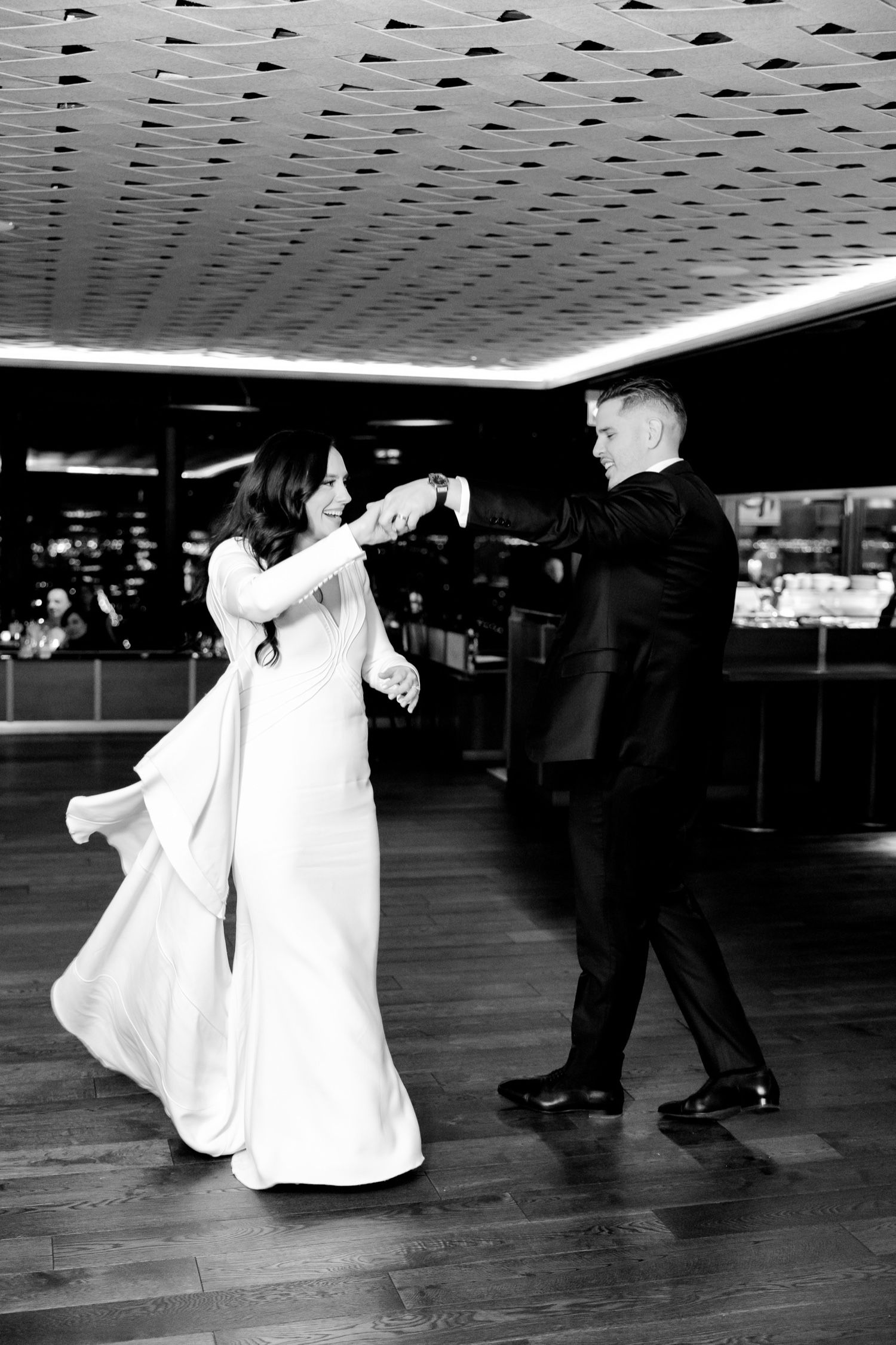 Elegant dancing couple twirling on wooden floor under geometric ceiling pattern.