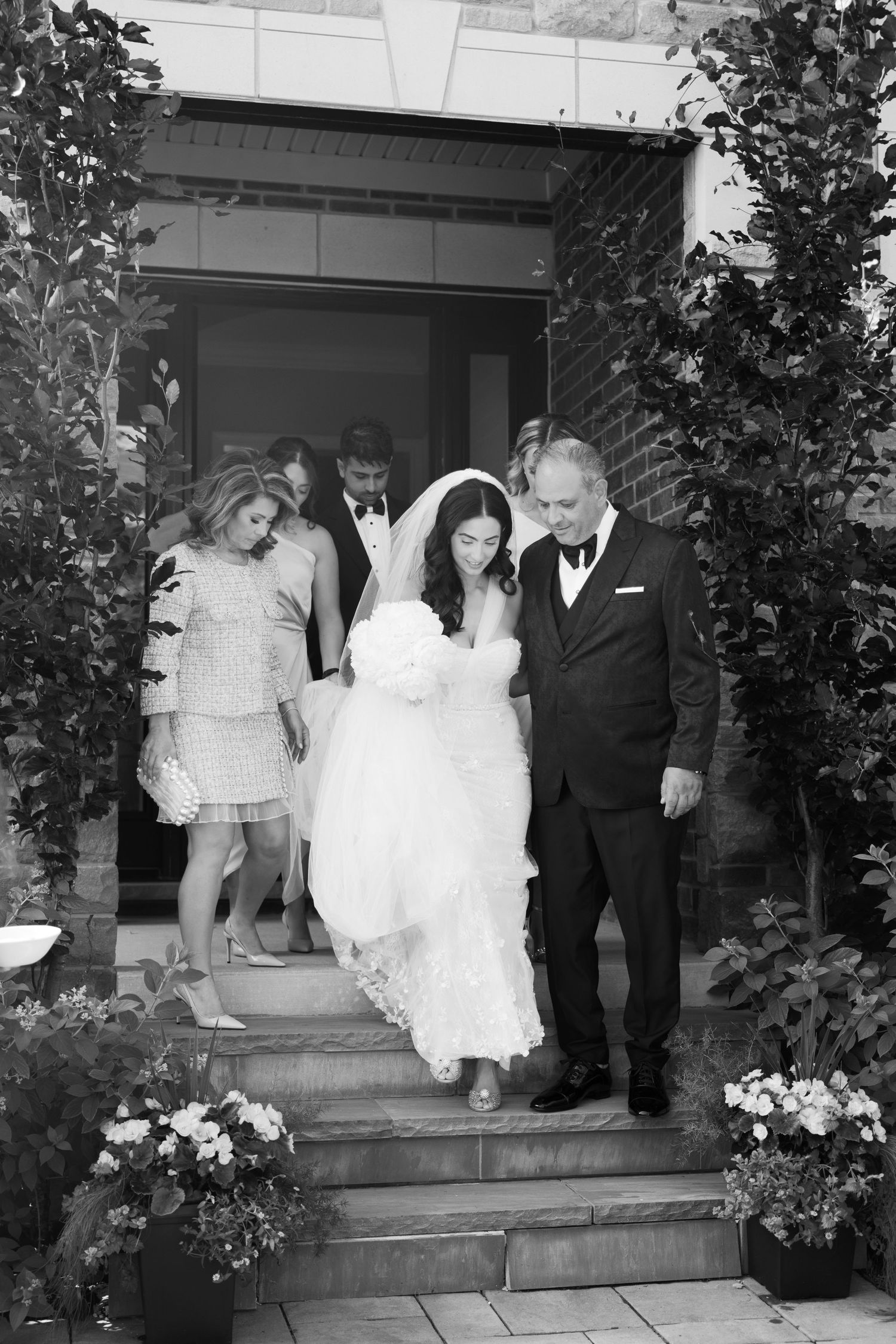 Black and white portrait of wedding party descending stone steps at entrance.