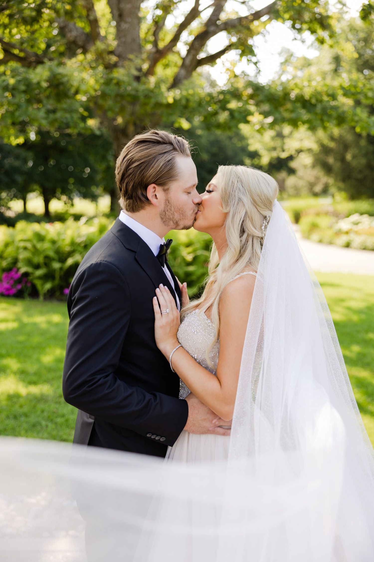 A tender moment between newlyweds sharing a kiss in a sunlit garden with a flowing white veil.