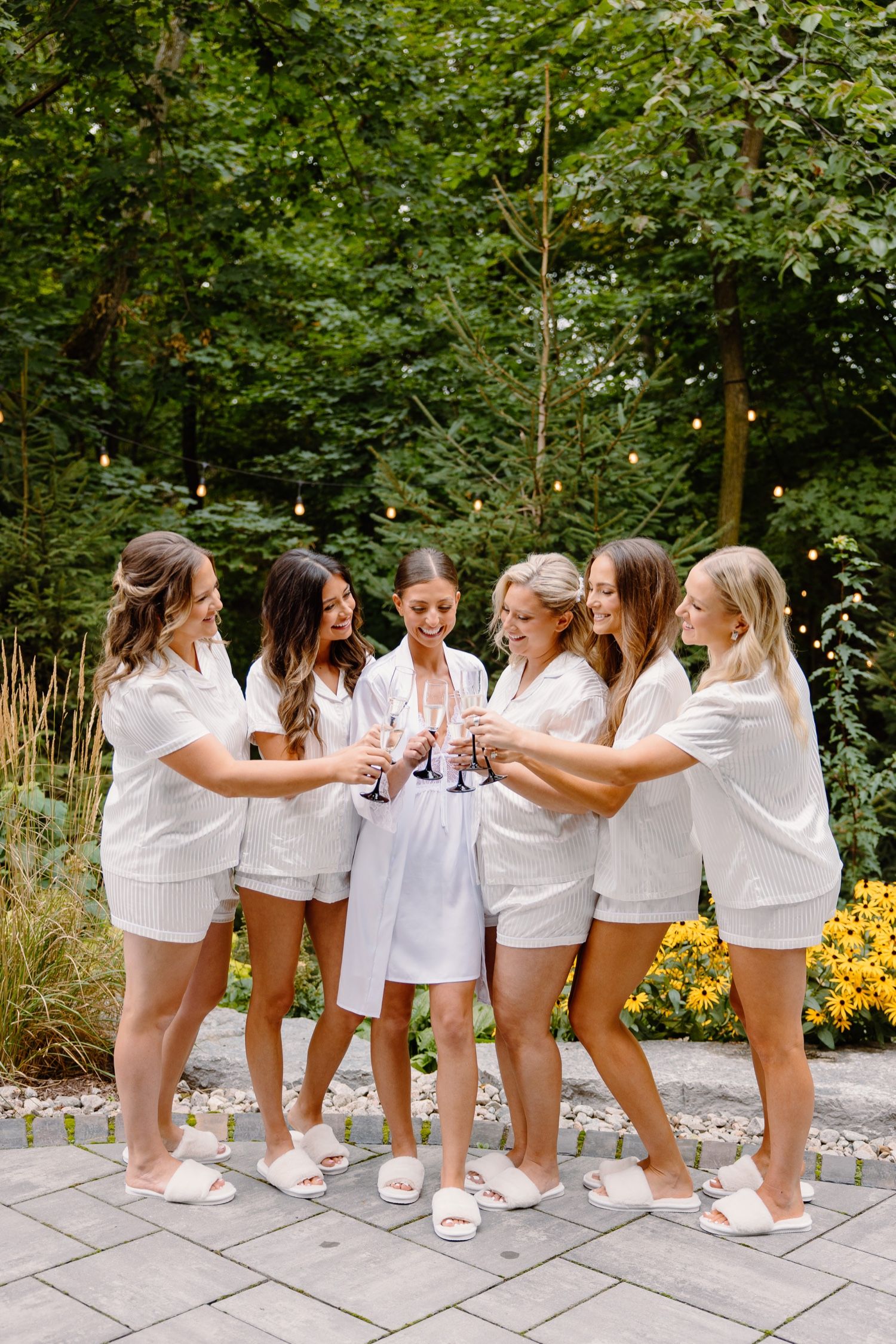 Festive gathering with champagne toast in matching white outfits against lush garden backdrop.