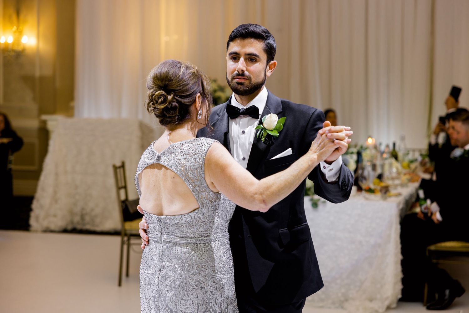 Couple dancing in elegant ballroom with formal attire and decorative lighting.