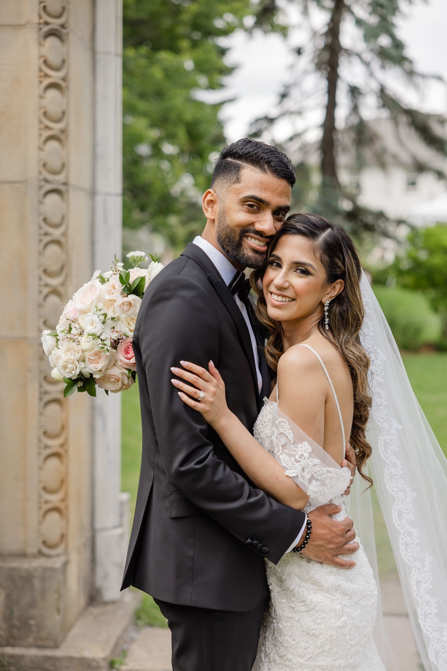A joyful wedding portrait captured at an ornate garden entrance with stone architecture.