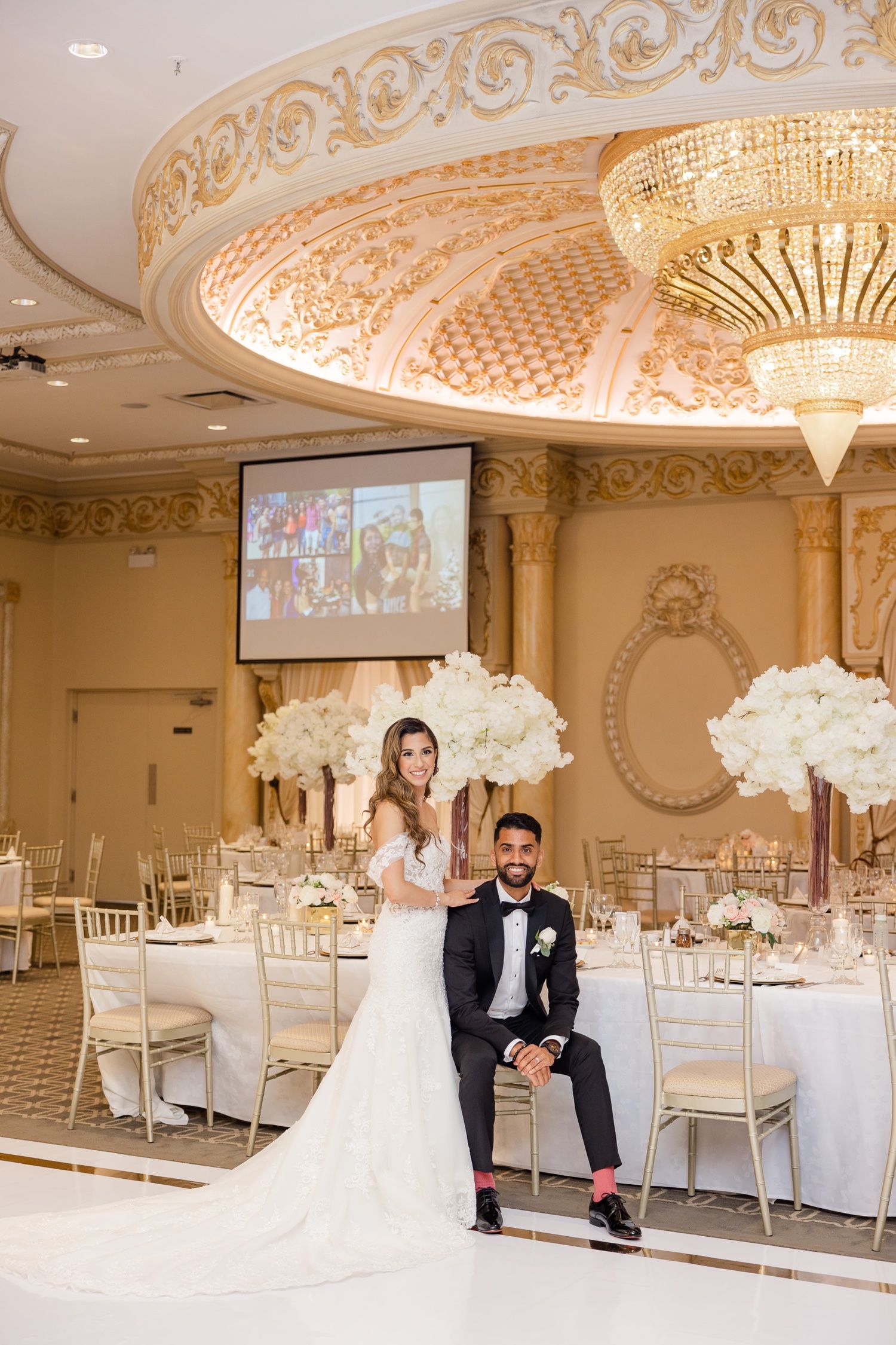 Elegant ballroom with ornate ceiling details, crystal chandelier and formal table settings for a wedding reception.