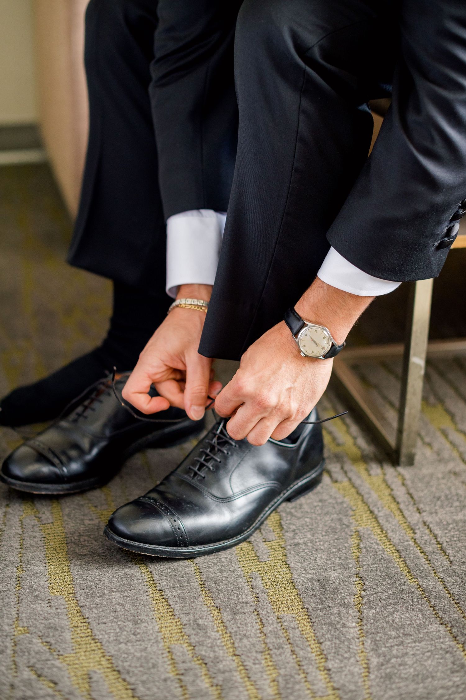 Close-up of hands tying formal black oxford dress shoes on carpeted floor.