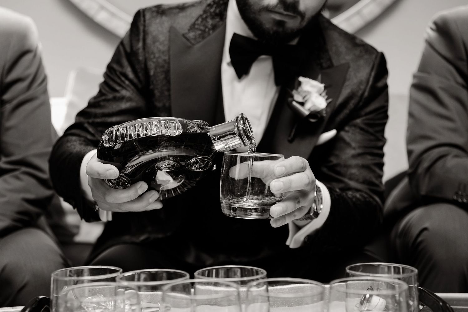 Black and white photo of someone pouring drinks from a bottle into glasses at a formal event.