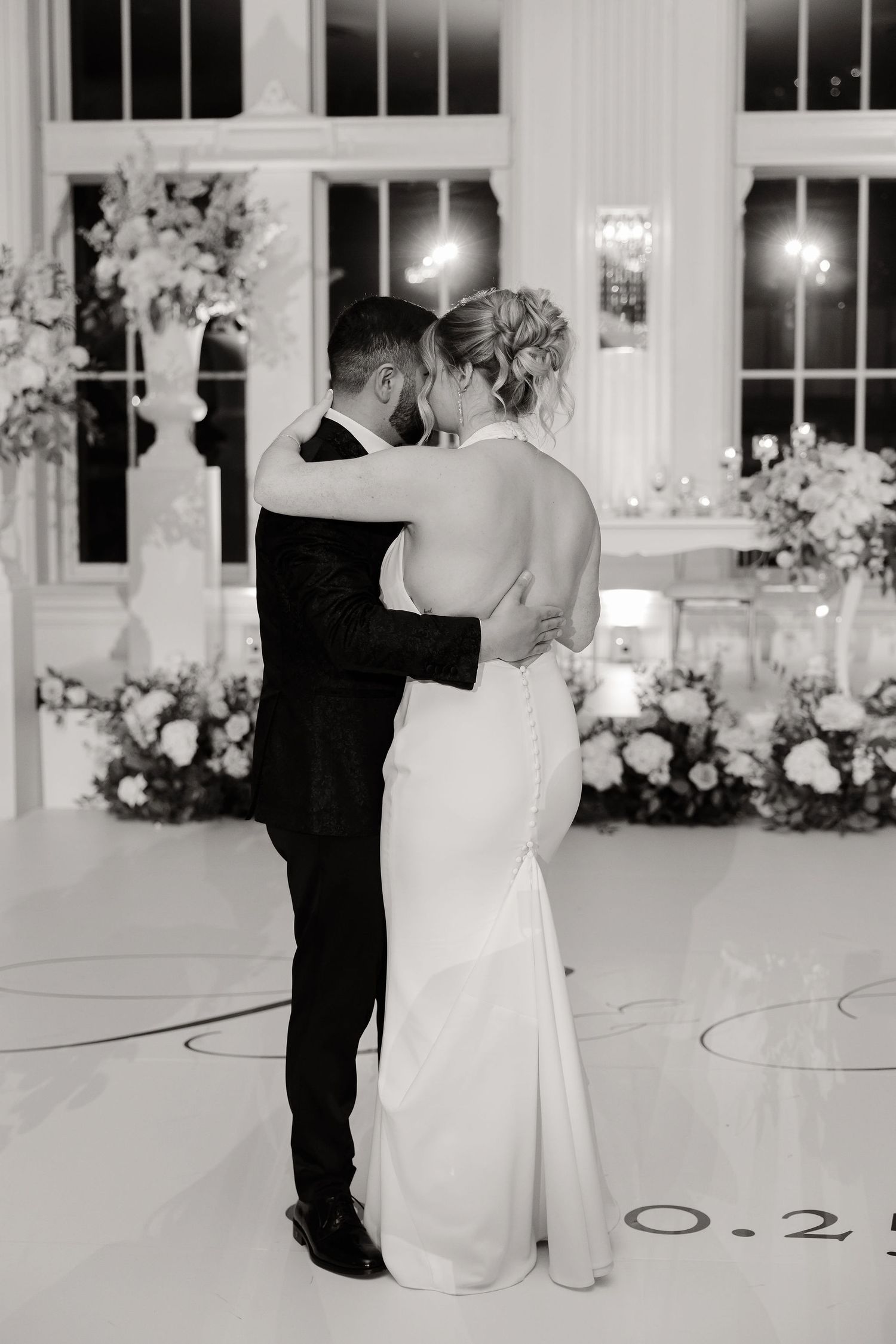 Black and white photo of a couple's first dance in an ornate reception hall with window lighting.