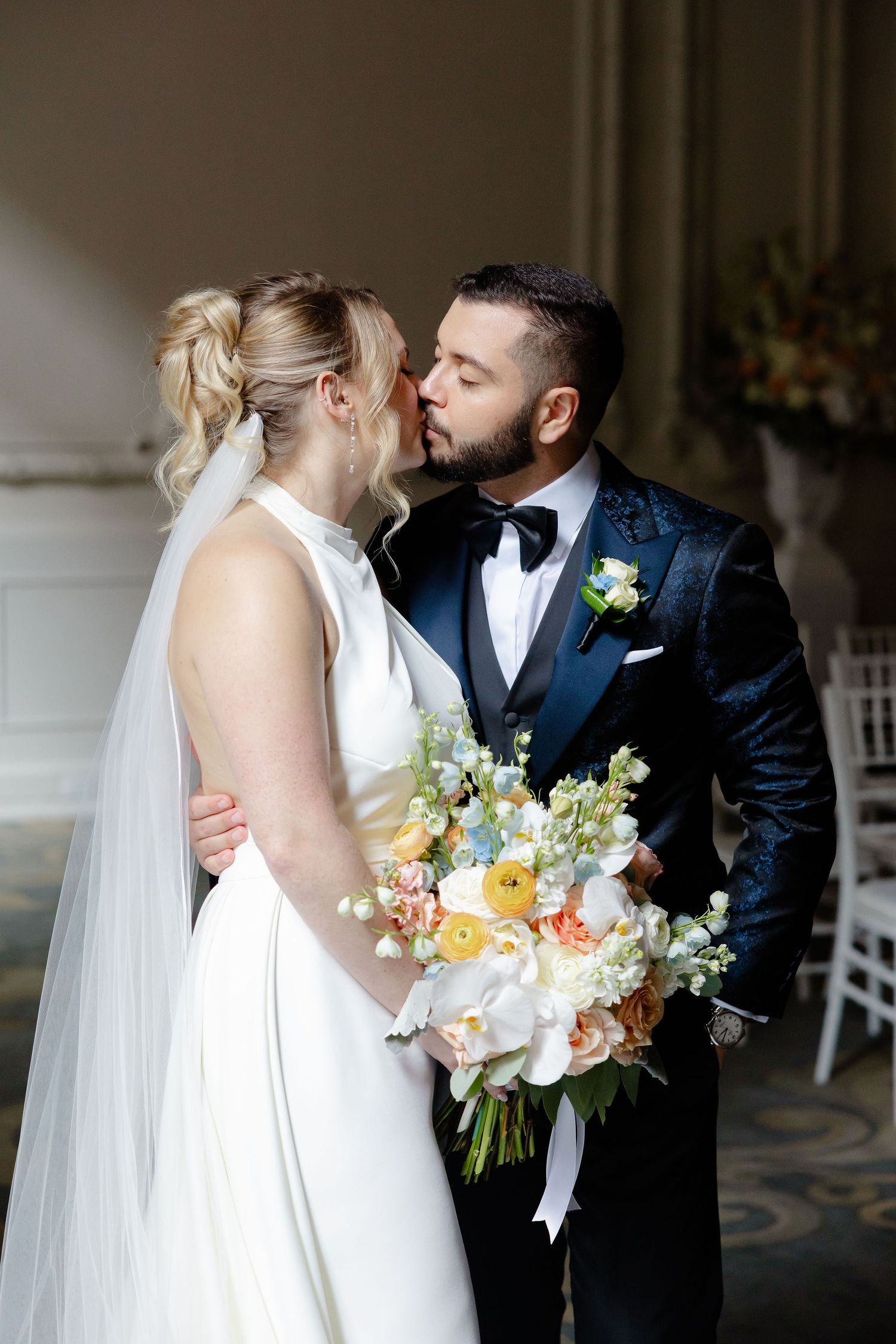 Intimate wedding couple embracing in front of ornate white walls holding a colorful spring bouquet.