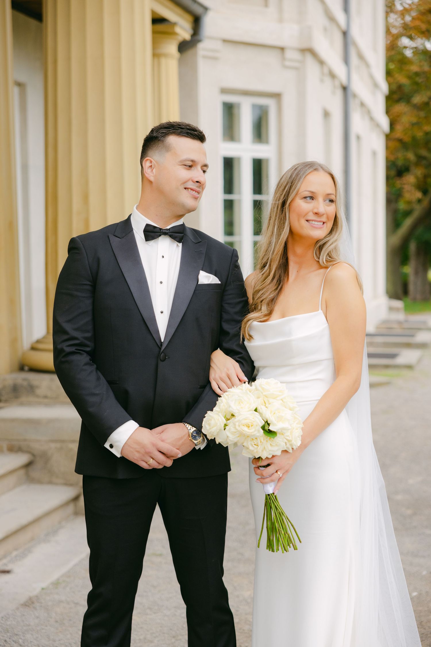 Wedding couple poses together beside historic building with white columns.