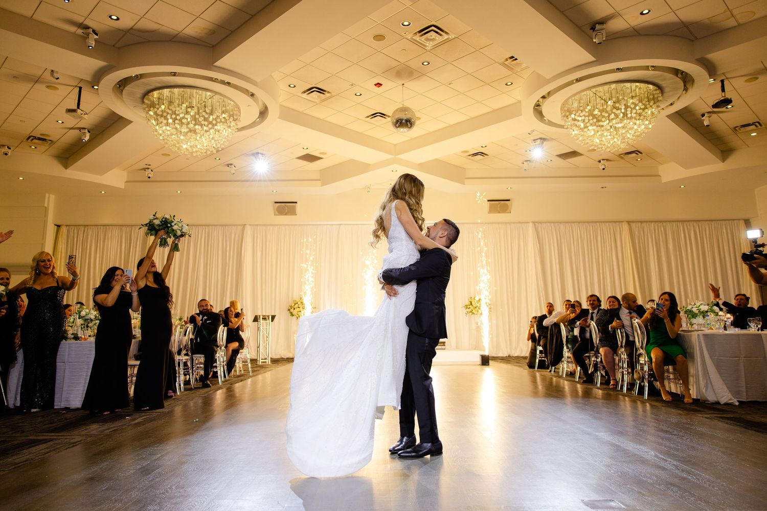 Elegant couple shares their first dance in beautifully lit ballroom with ornate ceiling medallions.