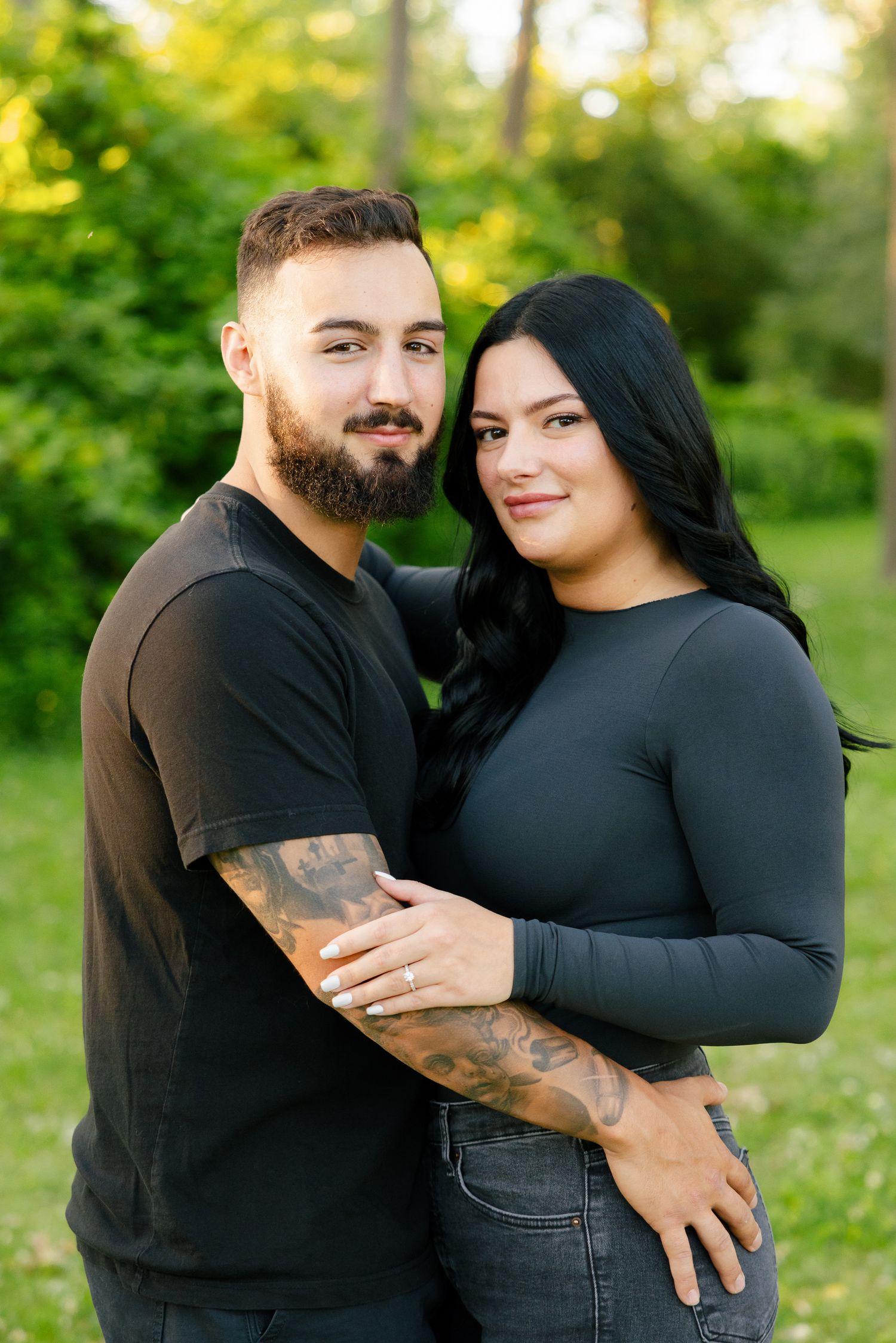 A couple poses together in a forest setting with beautiful golden hour lighting.