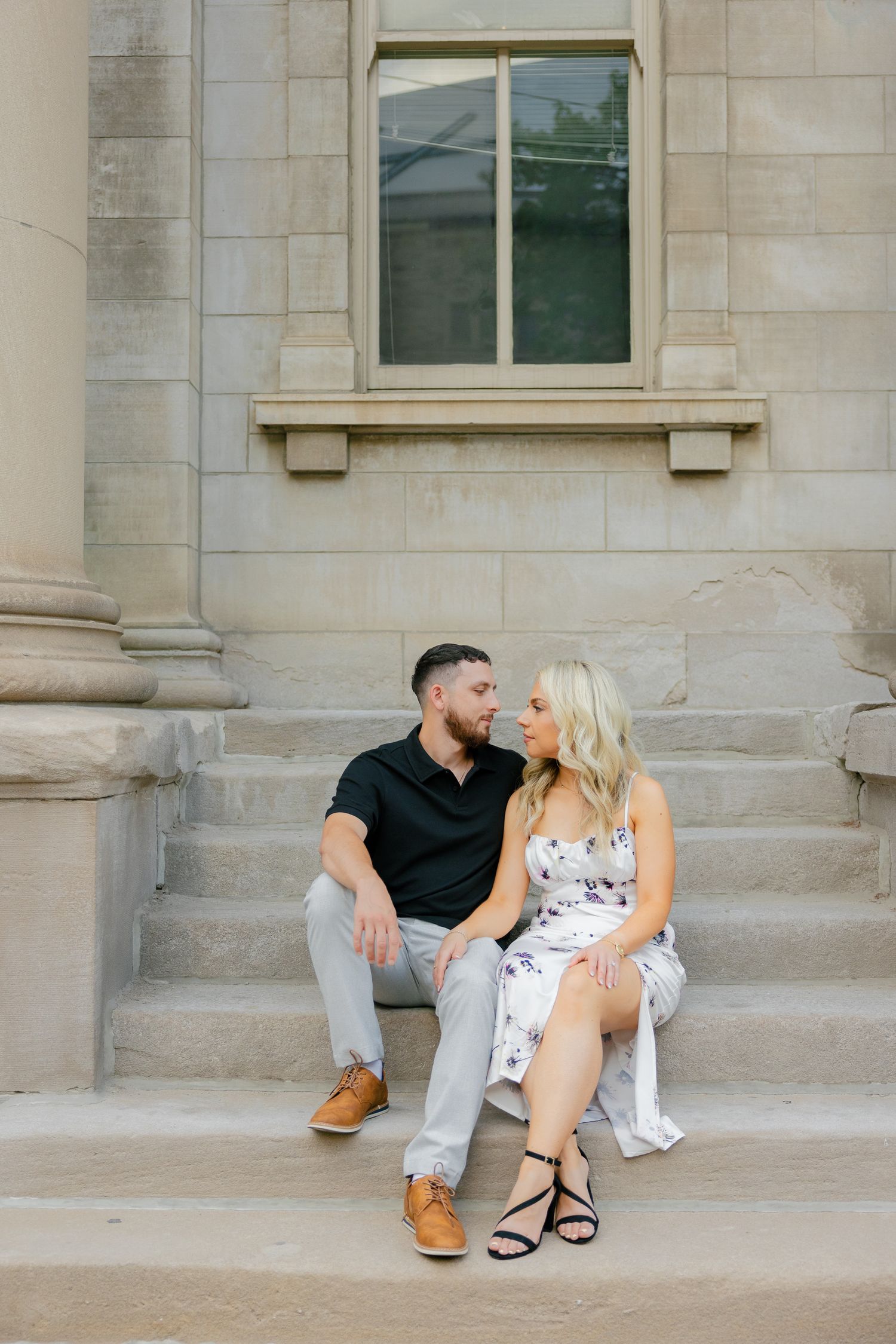 A tender moment shared between a couple seated on concrete steps of a classical building.