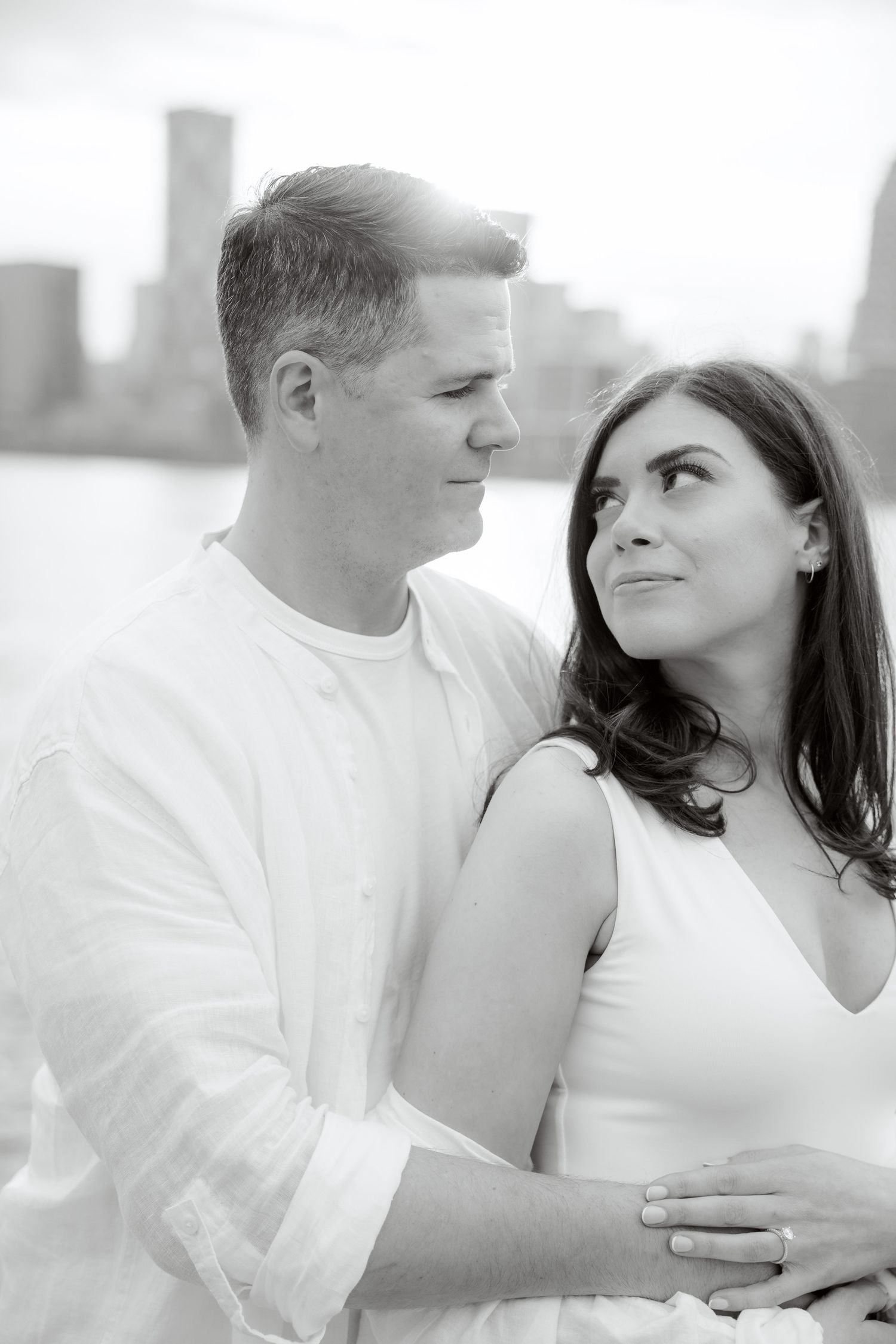A romantic portrait of a couple in white clothing posing against a city skyline backdrop.