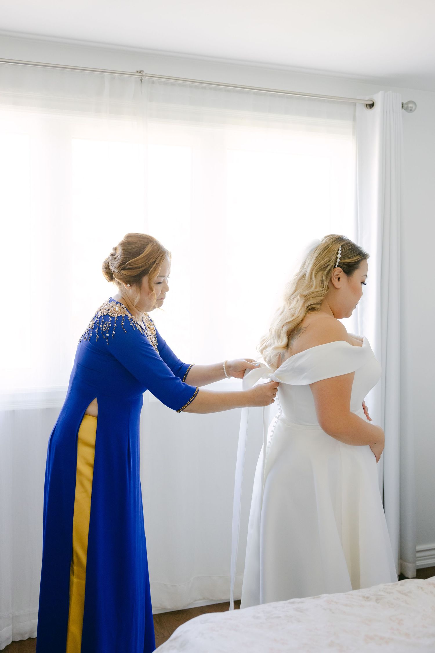 Wedding preparations with person in blue dress helping adjust white bridal gown.