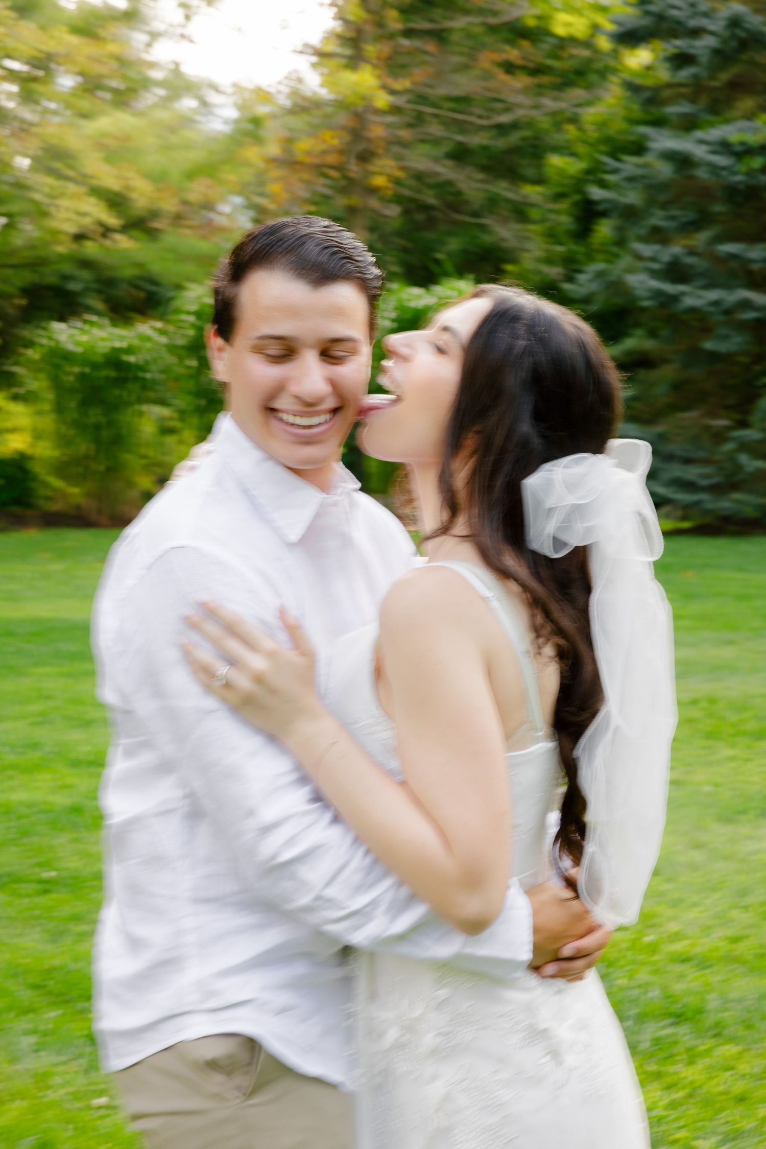 A romantic wedding couple laughing and embracing in a sunlit garden.