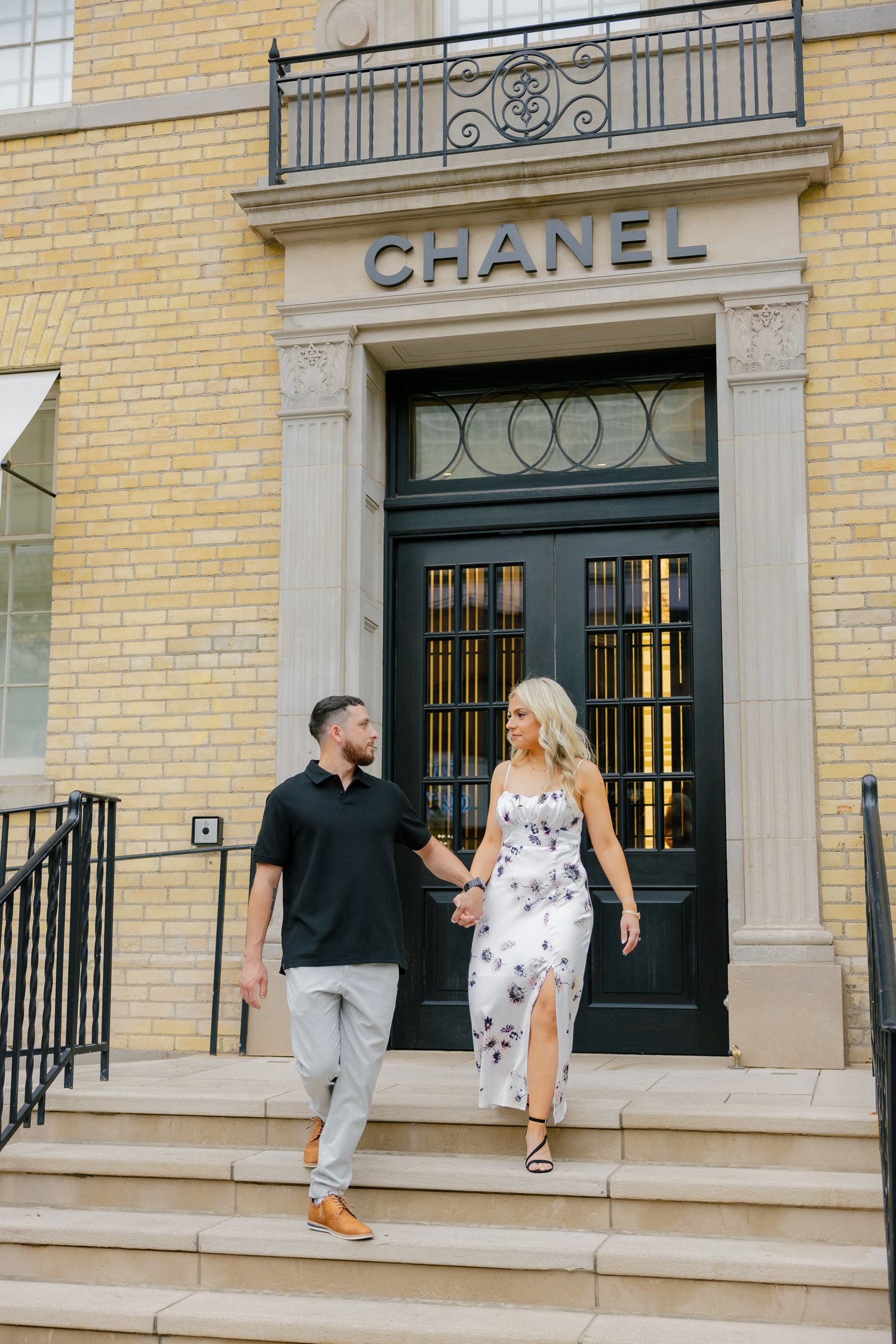 Couple descending stairs at Chanel store entrance in coordinated casual outfits.