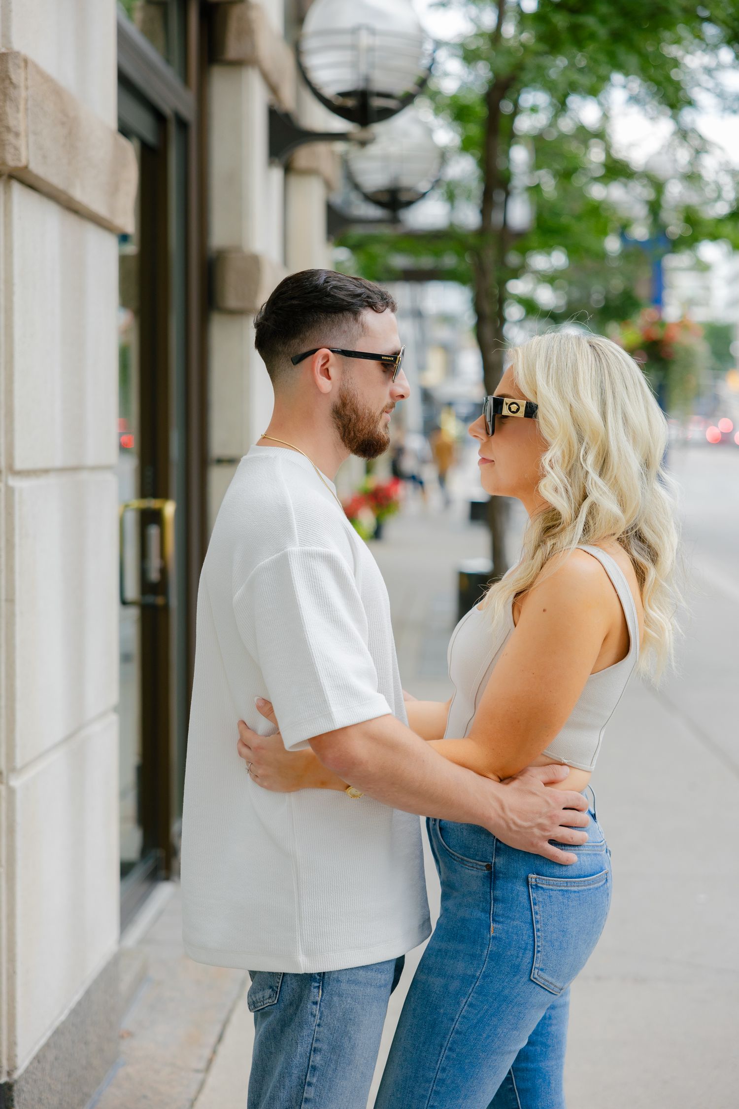 A couple shares an intimate moment on a city sidewalk with vintage street lamps.
