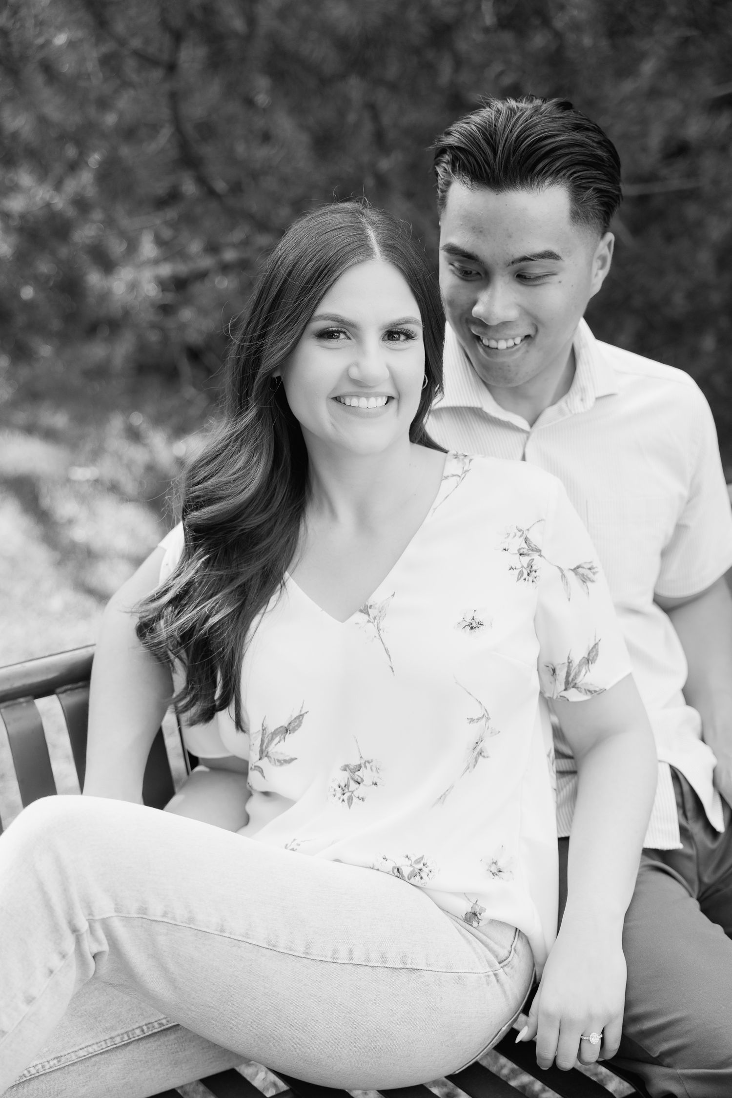 A romantic black and white portrait of a couple sitting together on a wooden bench outdoors.