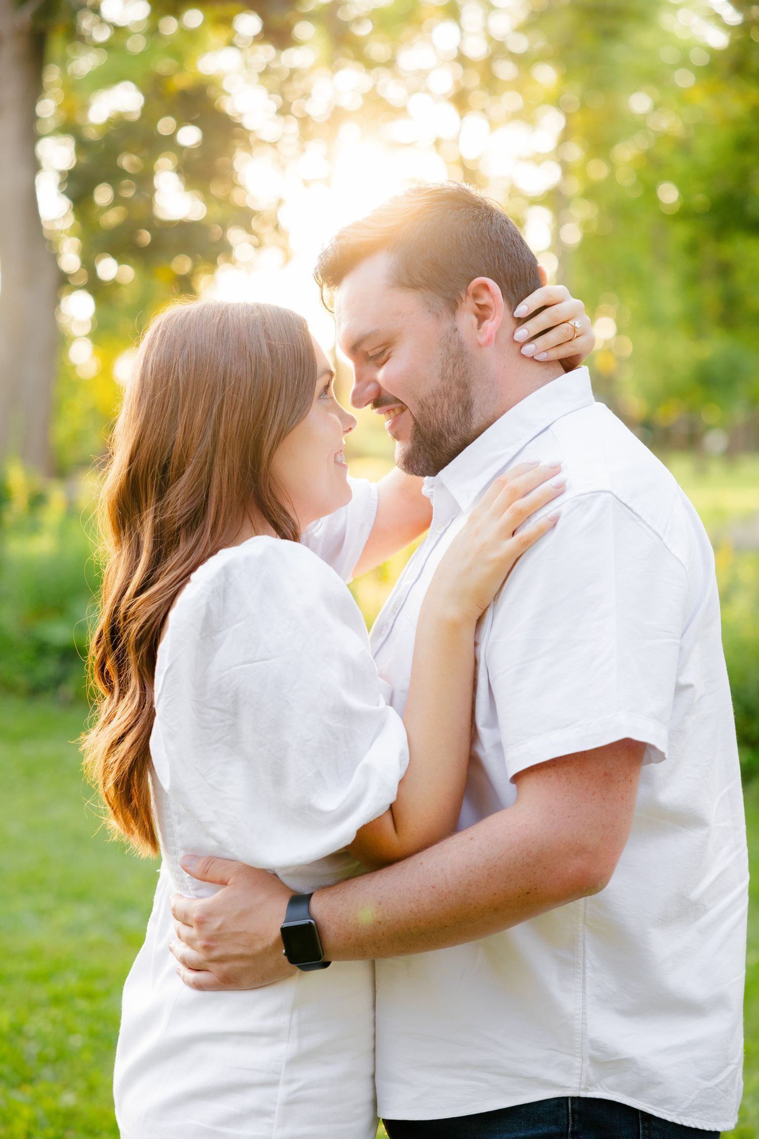 A couple in white embraces tenderly in a sunlit garden setting during golden hour.