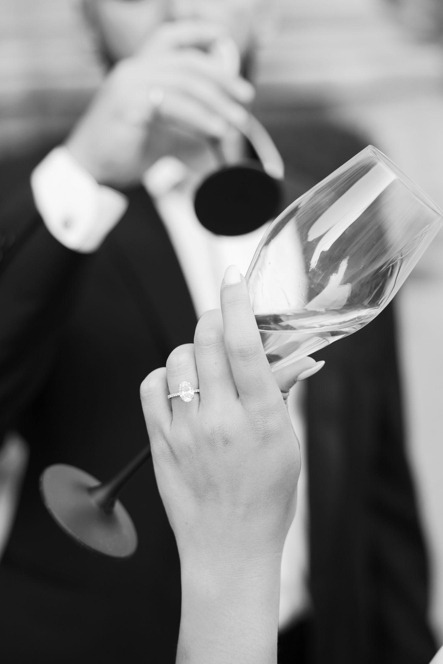 Detail shot of hand holding wine glass with engagement ring visible.