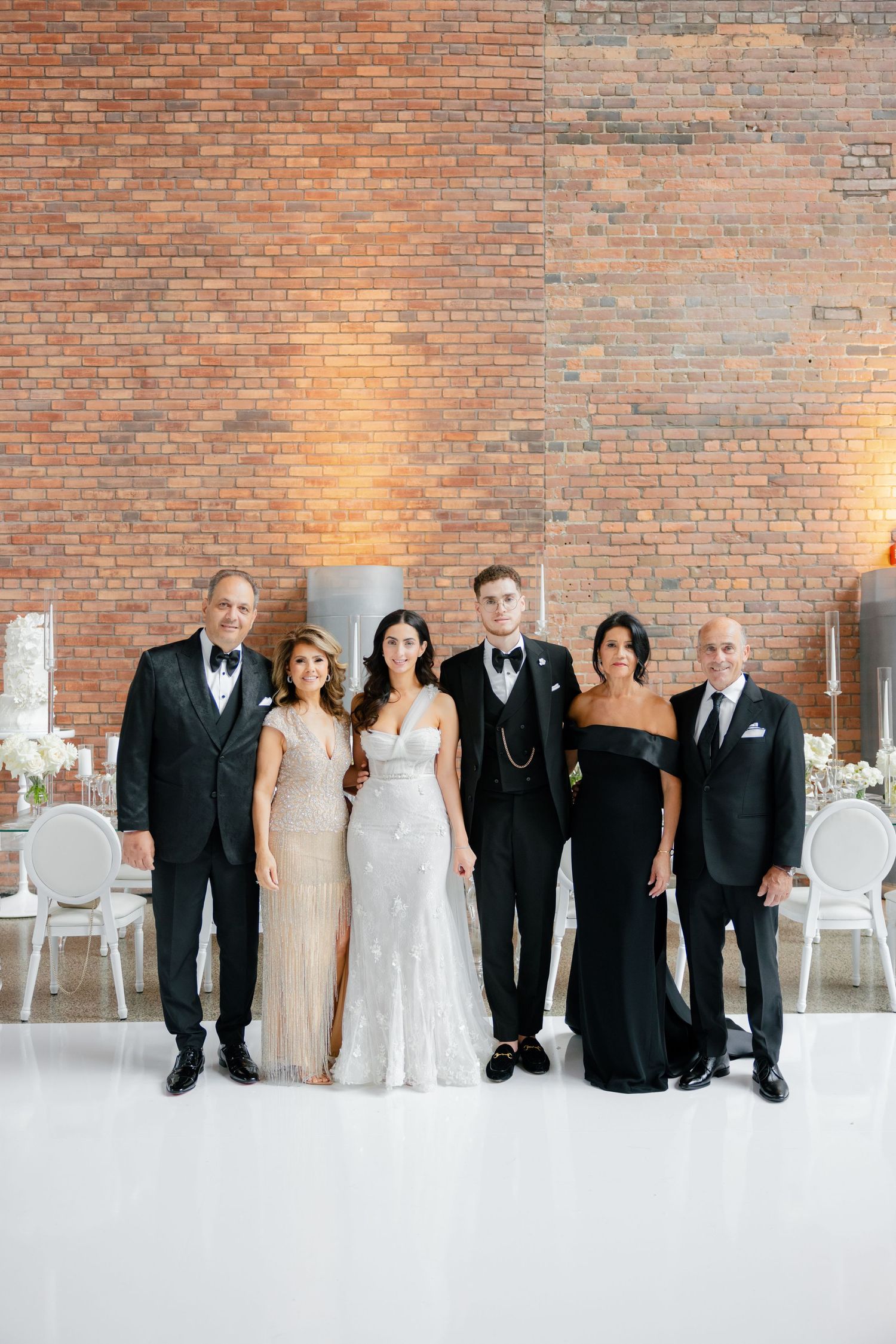Wedding party portrait with six people in formal evening wear against rustic brick backdrop.