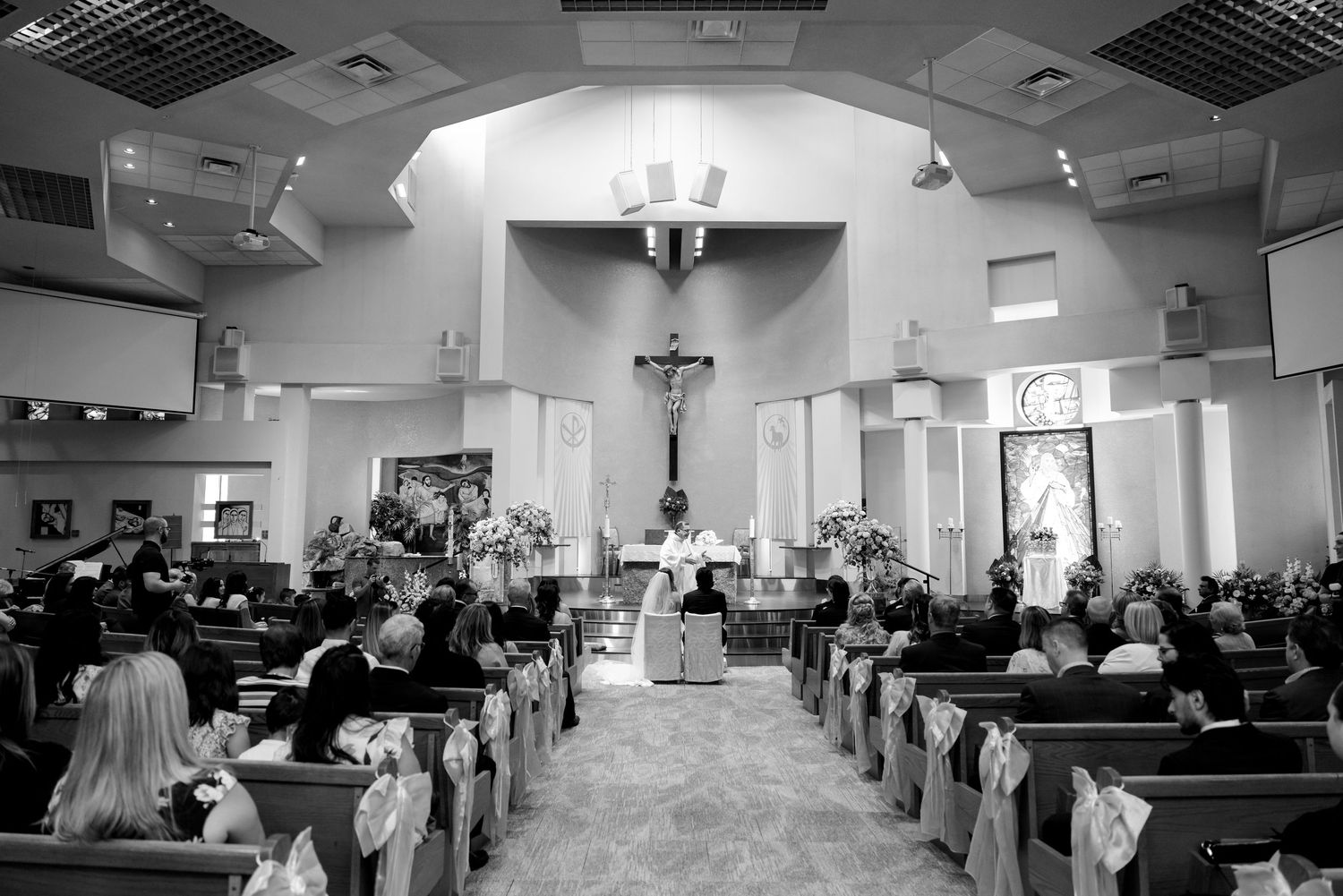 Black and white photograph of a wedding ceremony in a Catholic church with guests seated in wooden pews.